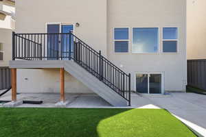 Rear exterior with a composite deck featuring black metal railings, a sliding glass door, and a lower-level concrete patio with a walk-out basement entrance