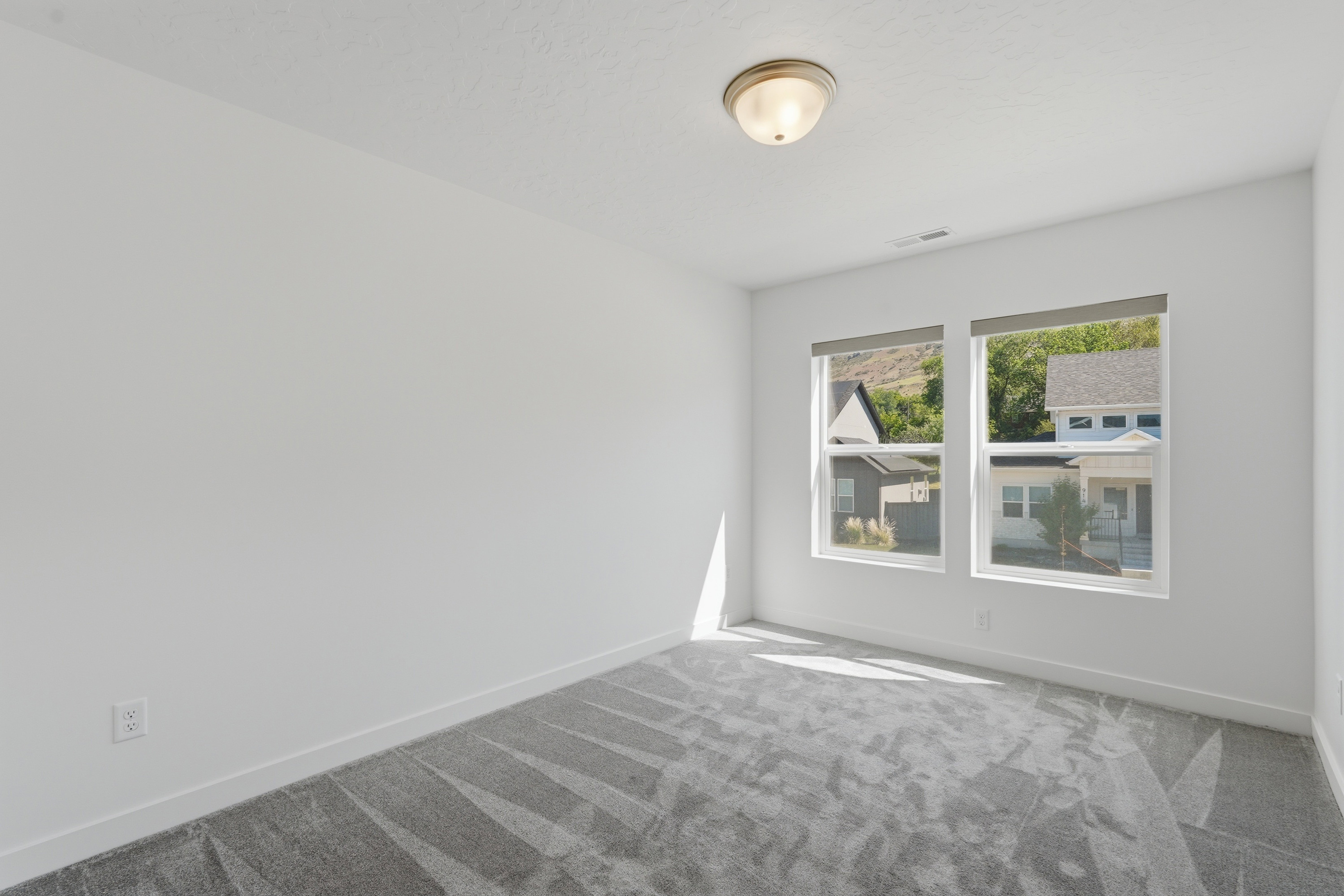 Spacious room featuring dual windows with roller shades, neutral white walls, and a patterned grey carpet