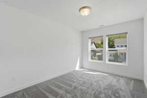 Spacious room featuring dual windows with roller shades, neutral white walls, and a patterned grey carpet