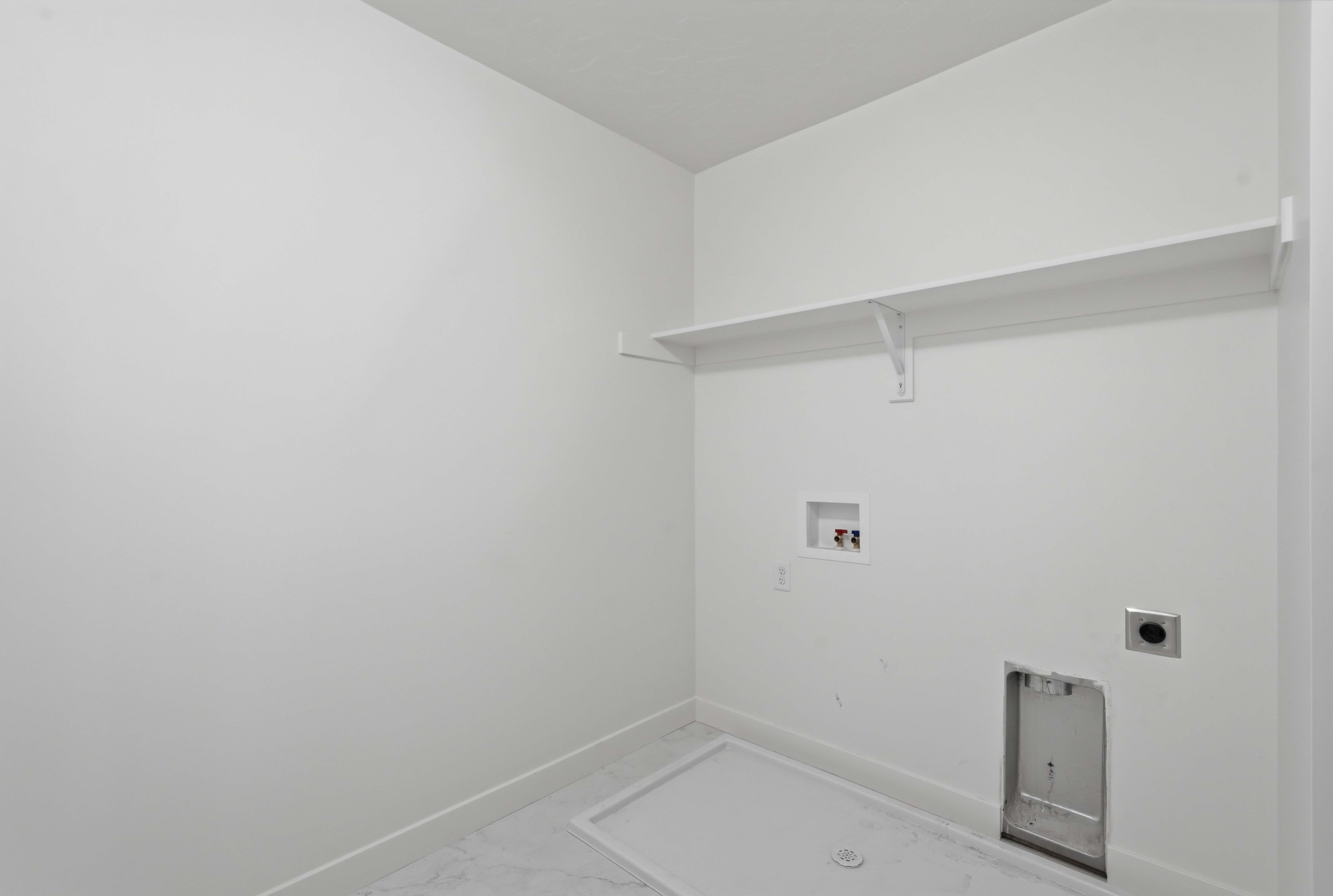 Dedicated laundry area featuring a white floating shelf, wall-mounted utility connections, and tile flooring