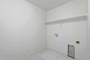 Dedicated laundry area featuring a white floating shelf, wall-mounted utility connections, and tile flooring