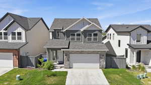 Modern-style home featuring a stone and siding facade, an attached two-car garage, multiple windows with dark framing, and a front entry with a white door