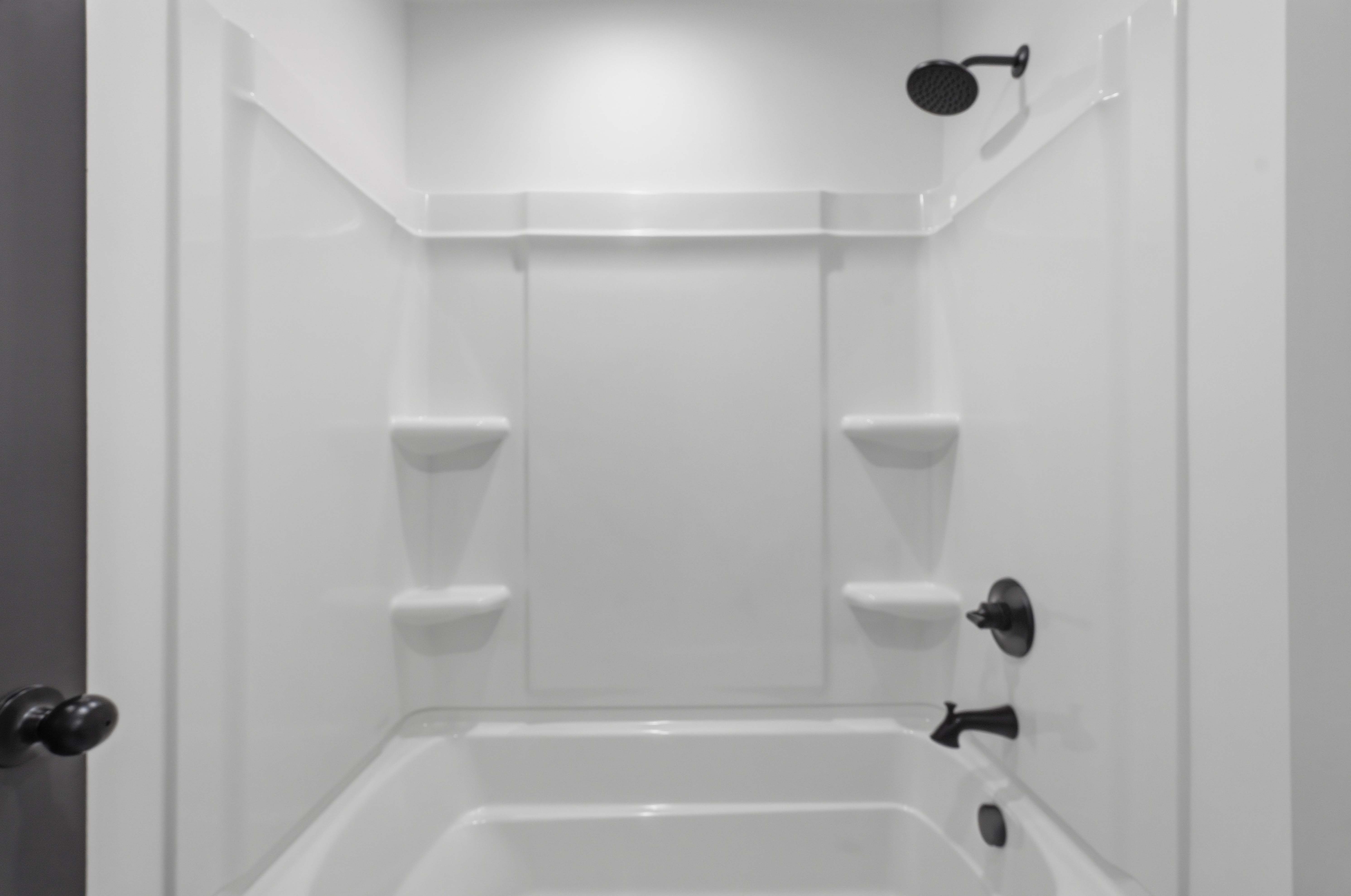 White bathtub and shower combination unit featuring integrated shelving and matte black fixtures