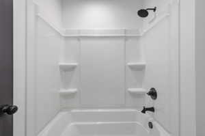 White bathtub and shower combination unit featuring integrated shelving and matte black fixtures
