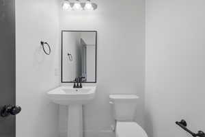 Pedestal sink with matte black faucet and coordinating mirror, complemented by a white toilet and modern light fixture