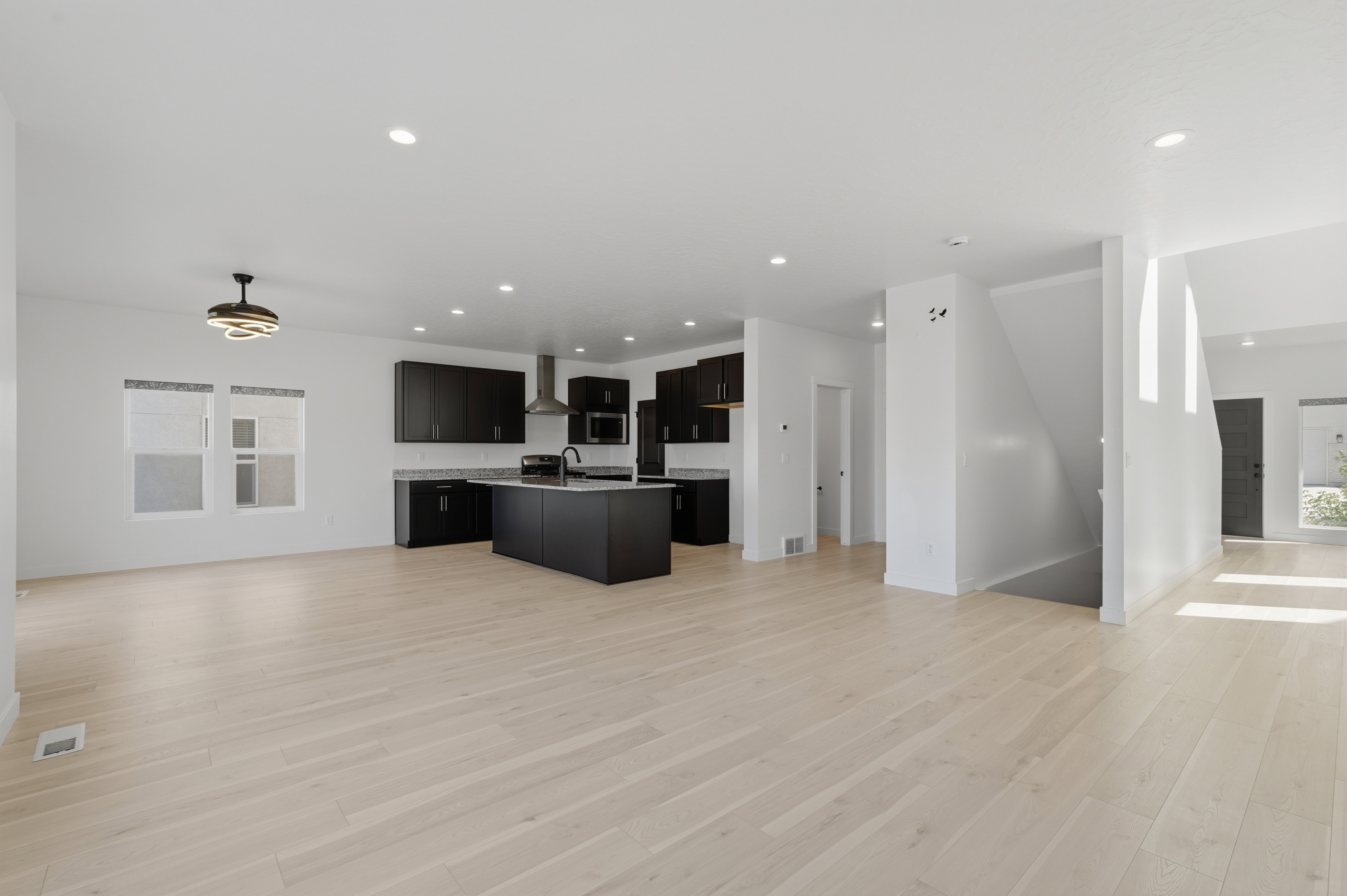 Open-concept living space featuring wood-finish flooring, recessed lighting, and a modern kitchen with dark cabinetry and stainless steel appliances