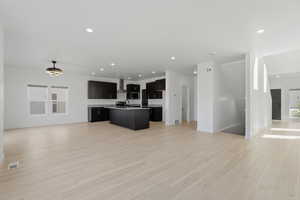 Open-concept living space featuring wood-finish flooring, recessed lighting, and a modern kitchen with dark cabinetry and stainless steel appliances