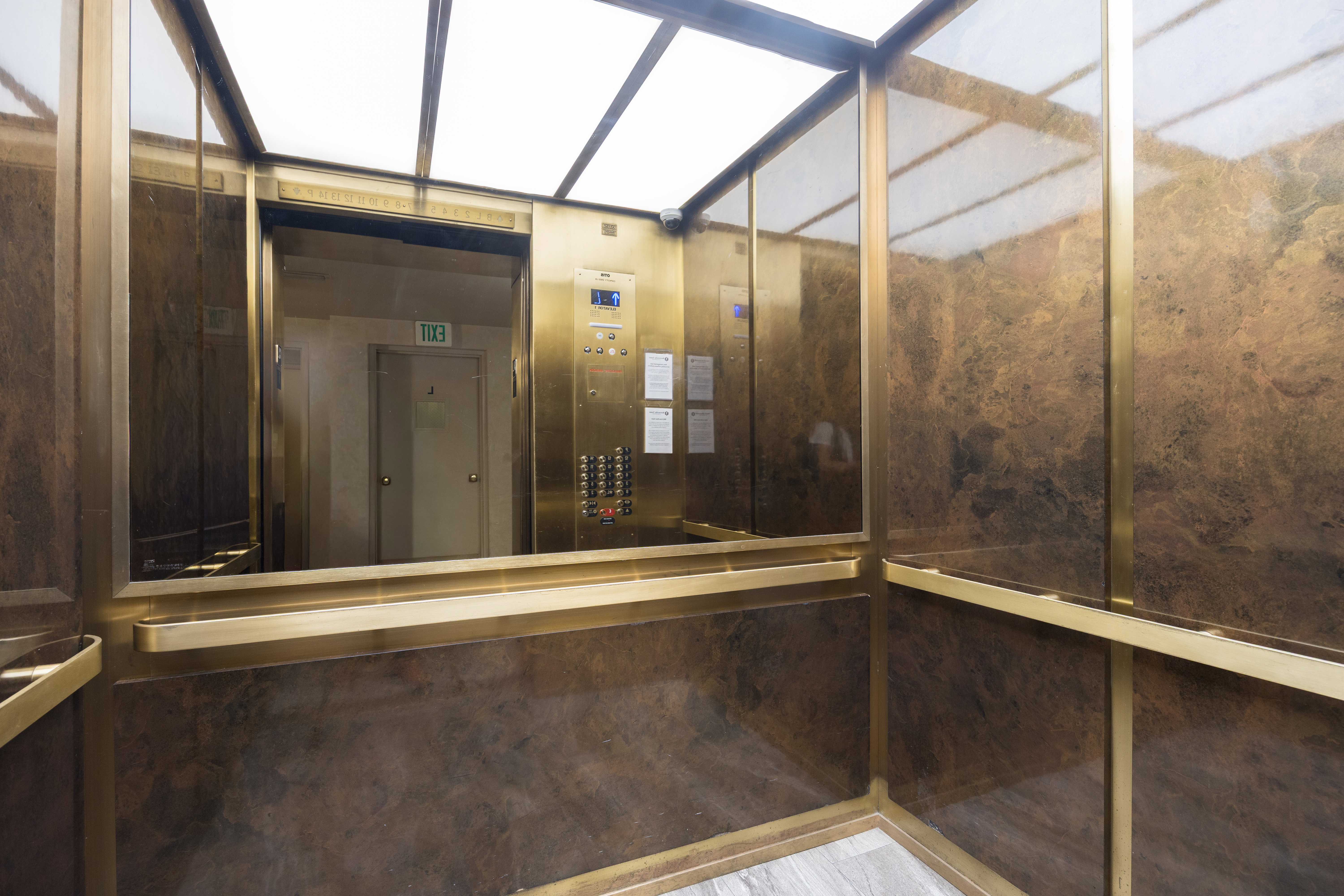 Elevator interior featuring brass accents, full-height mirror, stone-finish walls, and wood-finish flooring