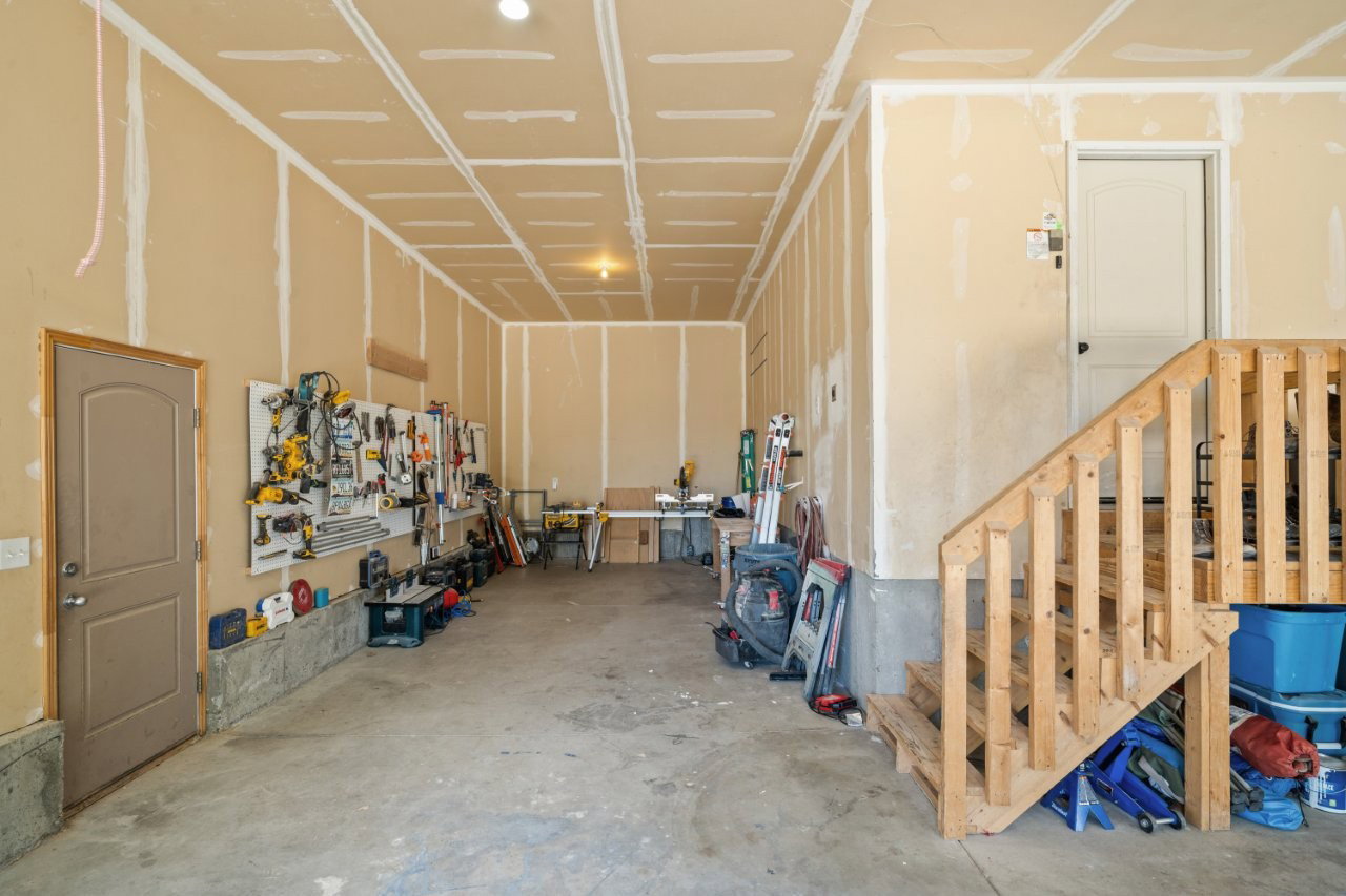 Spacious garage featuring unfinished walls, exposed ceiling joists, a concrete floor, and a wooden staircase