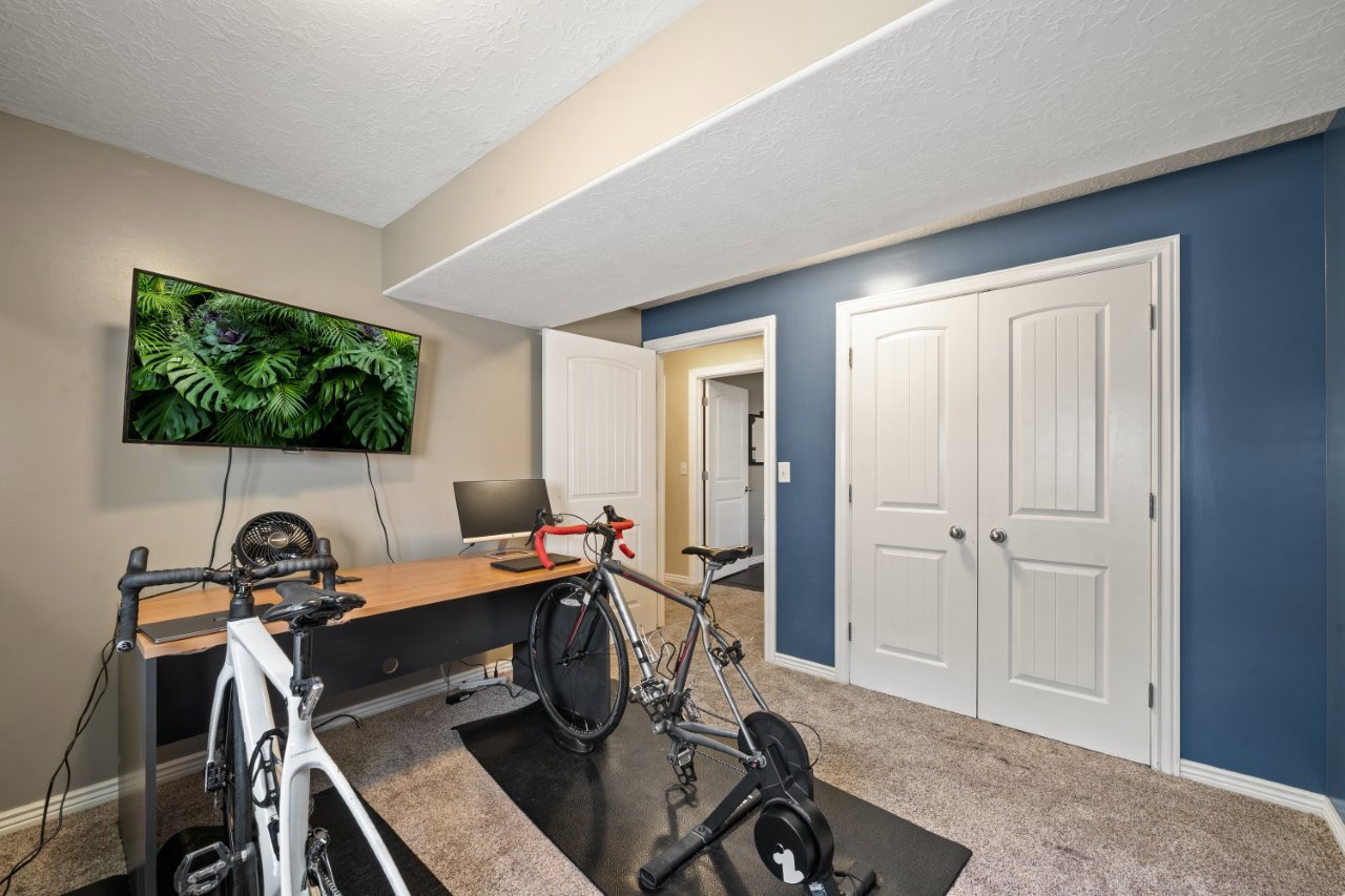 Versatile room featuring plush carpeting, a built-in wood-finish desk, and a mounted television
