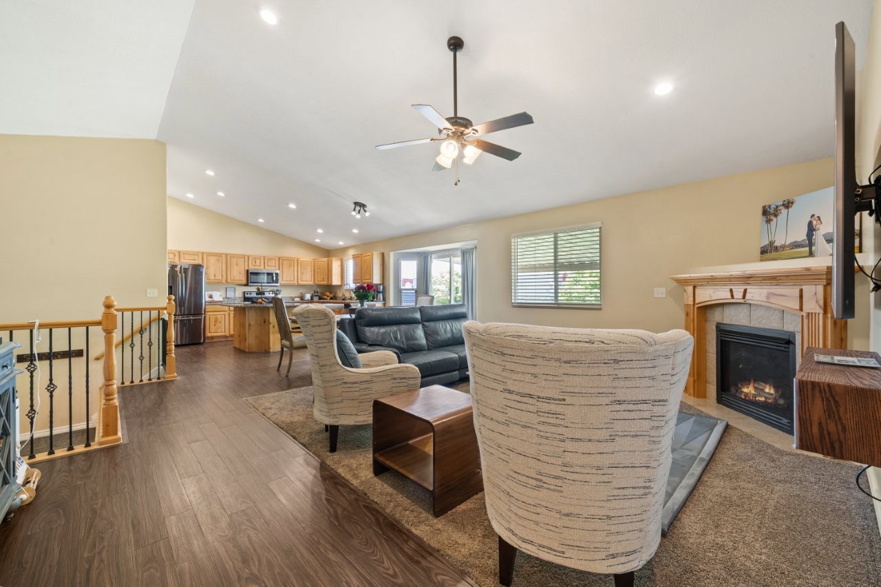 Vaulted ceiling living area featuring wood-finish flooring and a corner gas fireplace with wood mantel