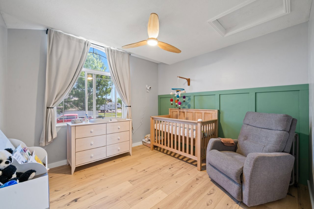 Room featuring wood-finish flooring, a decorative green wainscoting accent wall, a ceiling fan with integrated lighting, and a large arched window with drapery