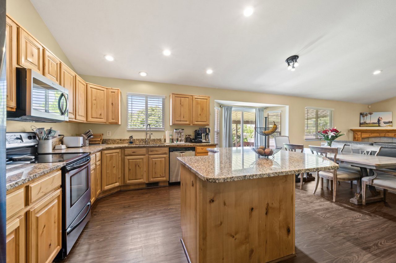Open-concept kitchen featuring light wood cabinetry, stainless steel appliances, granite countertops, and wood-finish flooring
