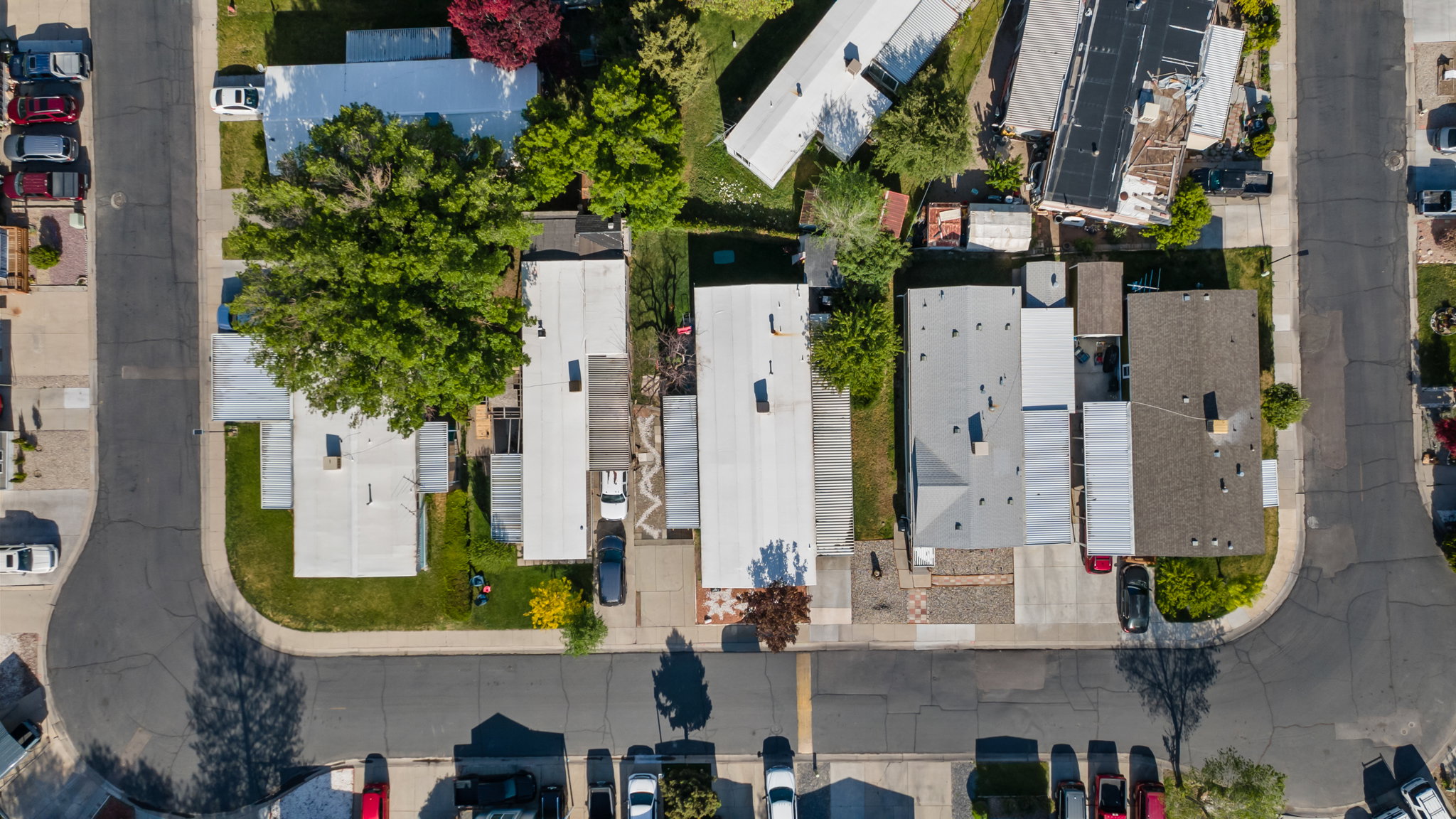 Aerial perspective of a residential street with multiple properties featuring mature trees and paved driveways