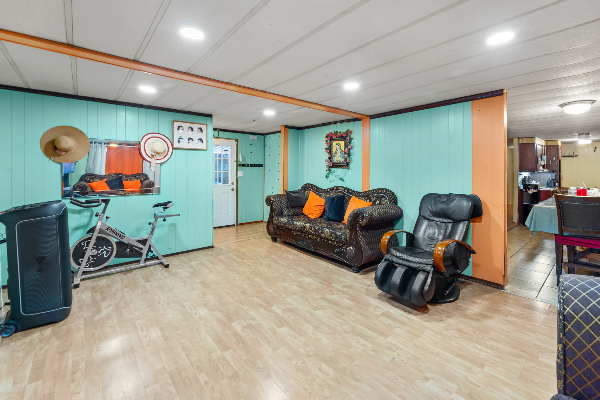 Spacious room featuring light wood-finish flooring, a white paneled ceiling with recessed lighting, and bright turquoise wall paneling