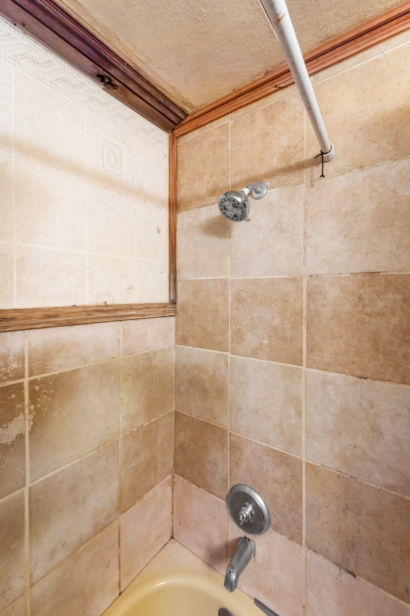 Tub and shower surround featuring earth-toned square tiles and a chrome shower head with a matching faucet