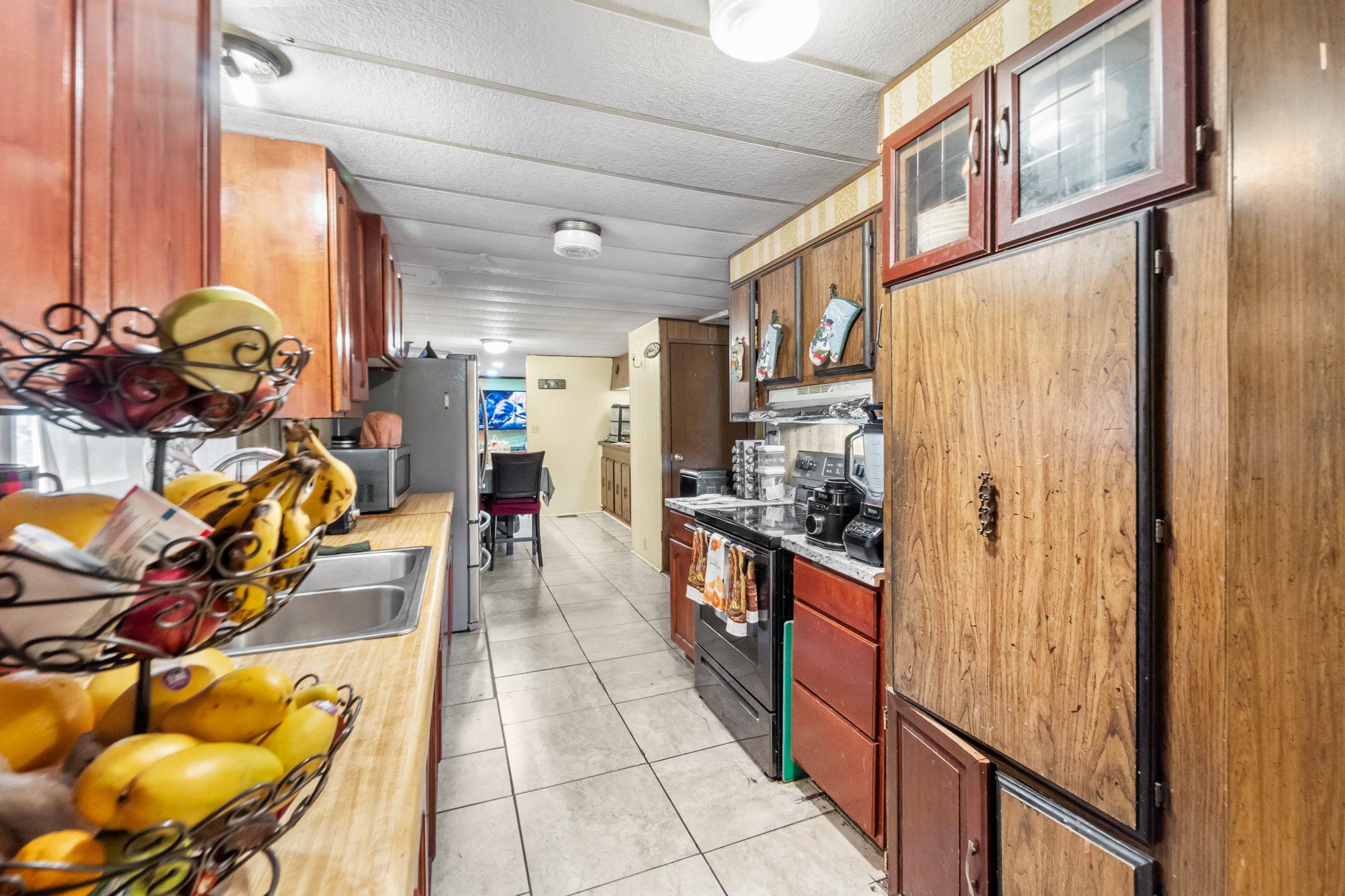 Galley kitchen featuring wood-finish cabinetry, a double basin stainless steel sink, a black electric range, and light-toned tile flooring