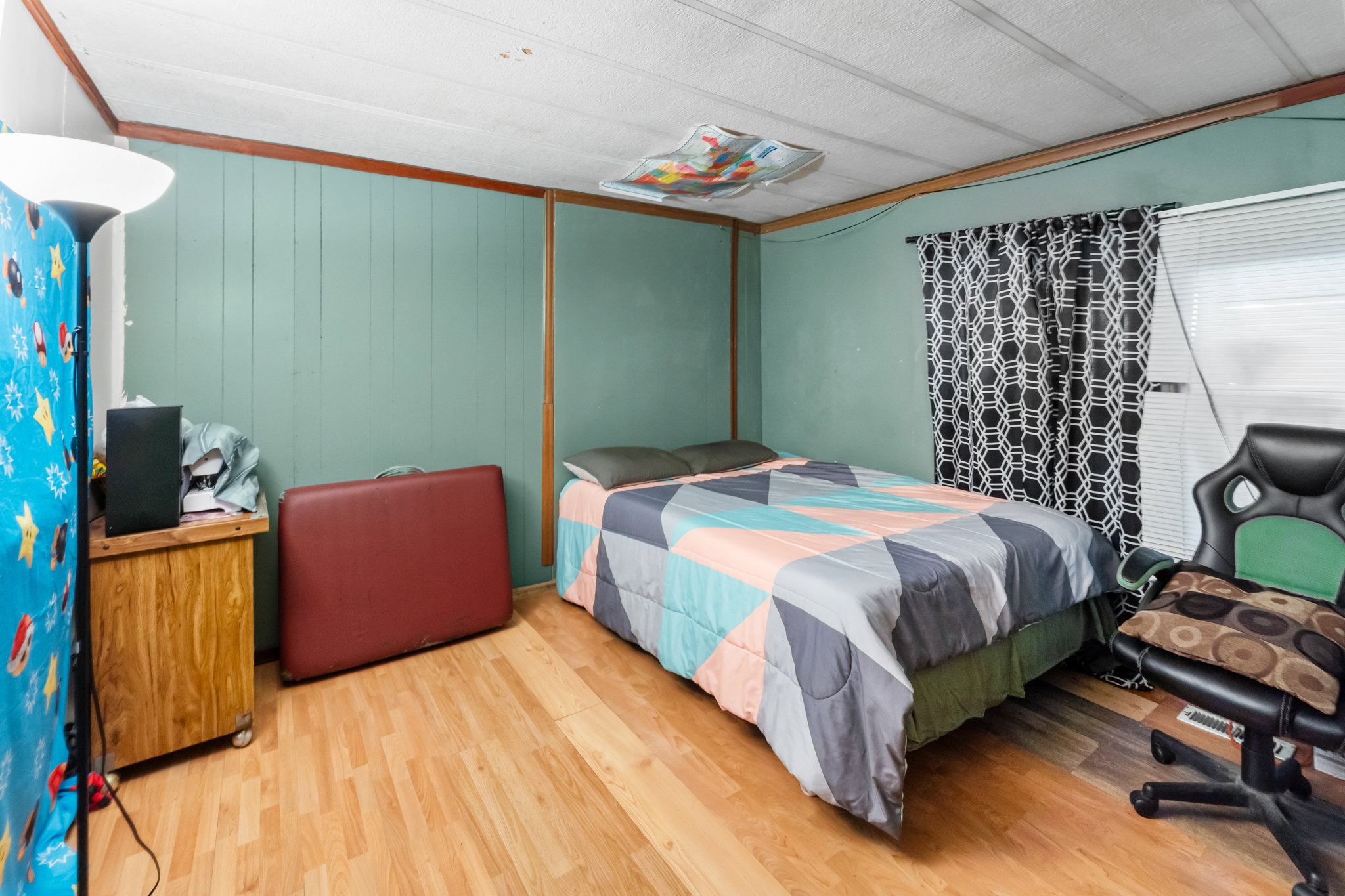 Interior room featuring wood-finish flooring, light teal wall paneling, and a large window with horizontal blinds