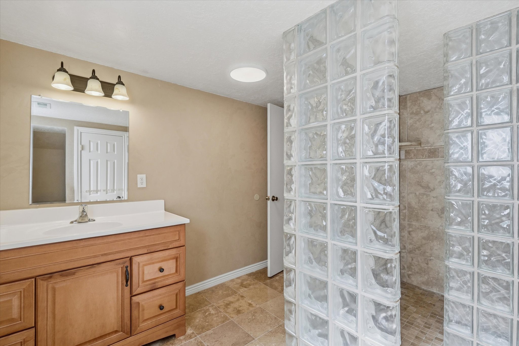 Bathroom featuring a light wood vanity with a white countertop and sink, a wall-mounted mirror, and a three-light fixture