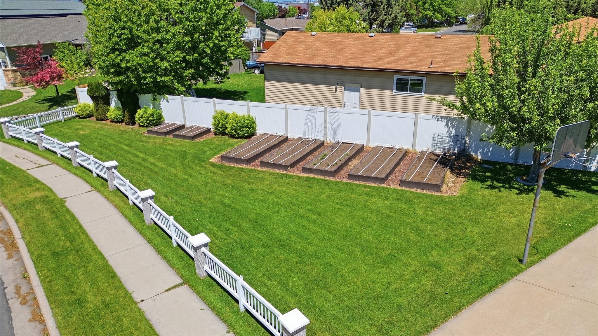 Expansive green lawn framed by a white picket fence and a privacy fence, and raised garden beds