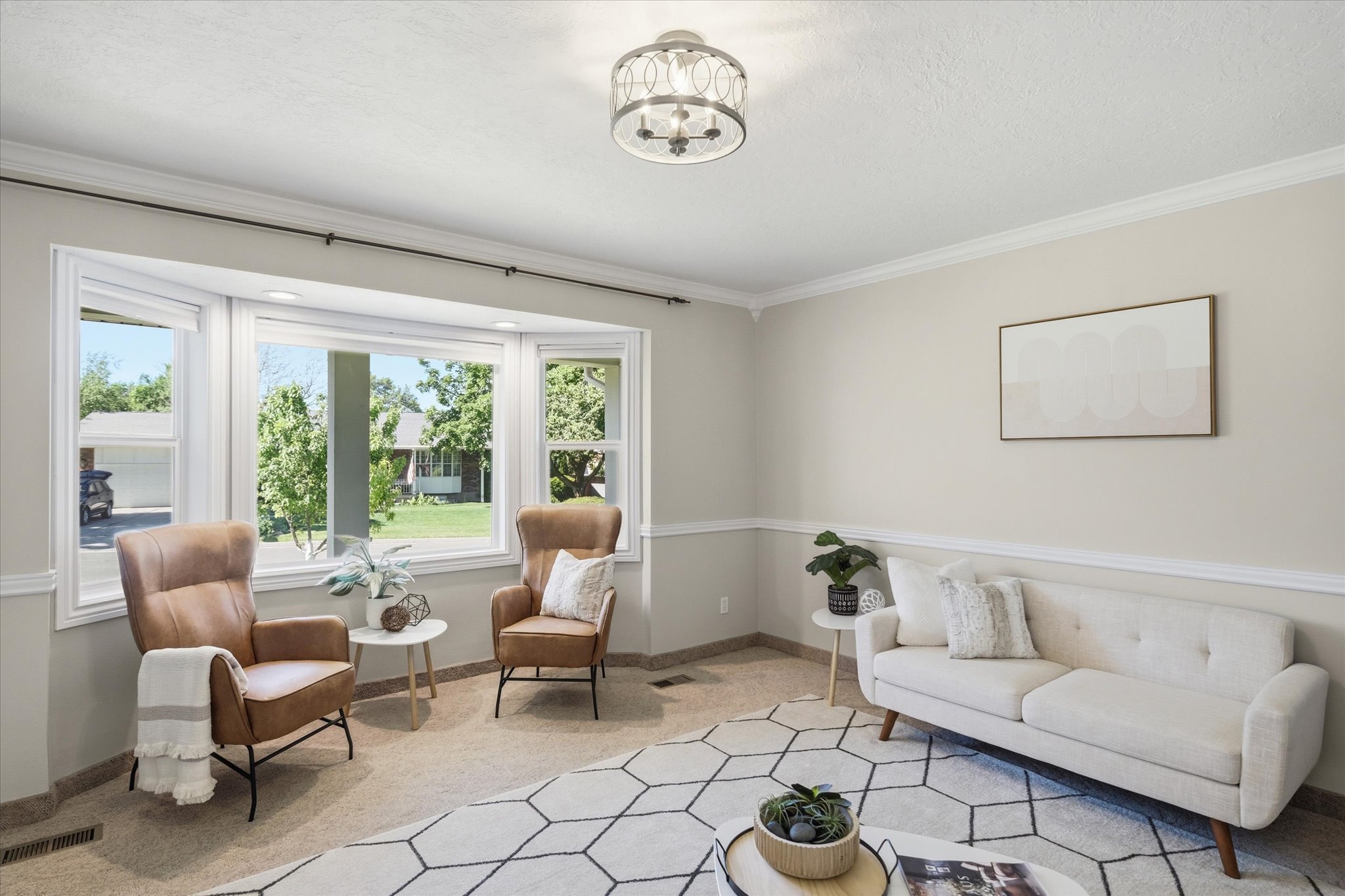 Spacious living area featuring a prominent bay window, crown molding, chair rail molding, a neutral color palette, and a ceiling light fixture
