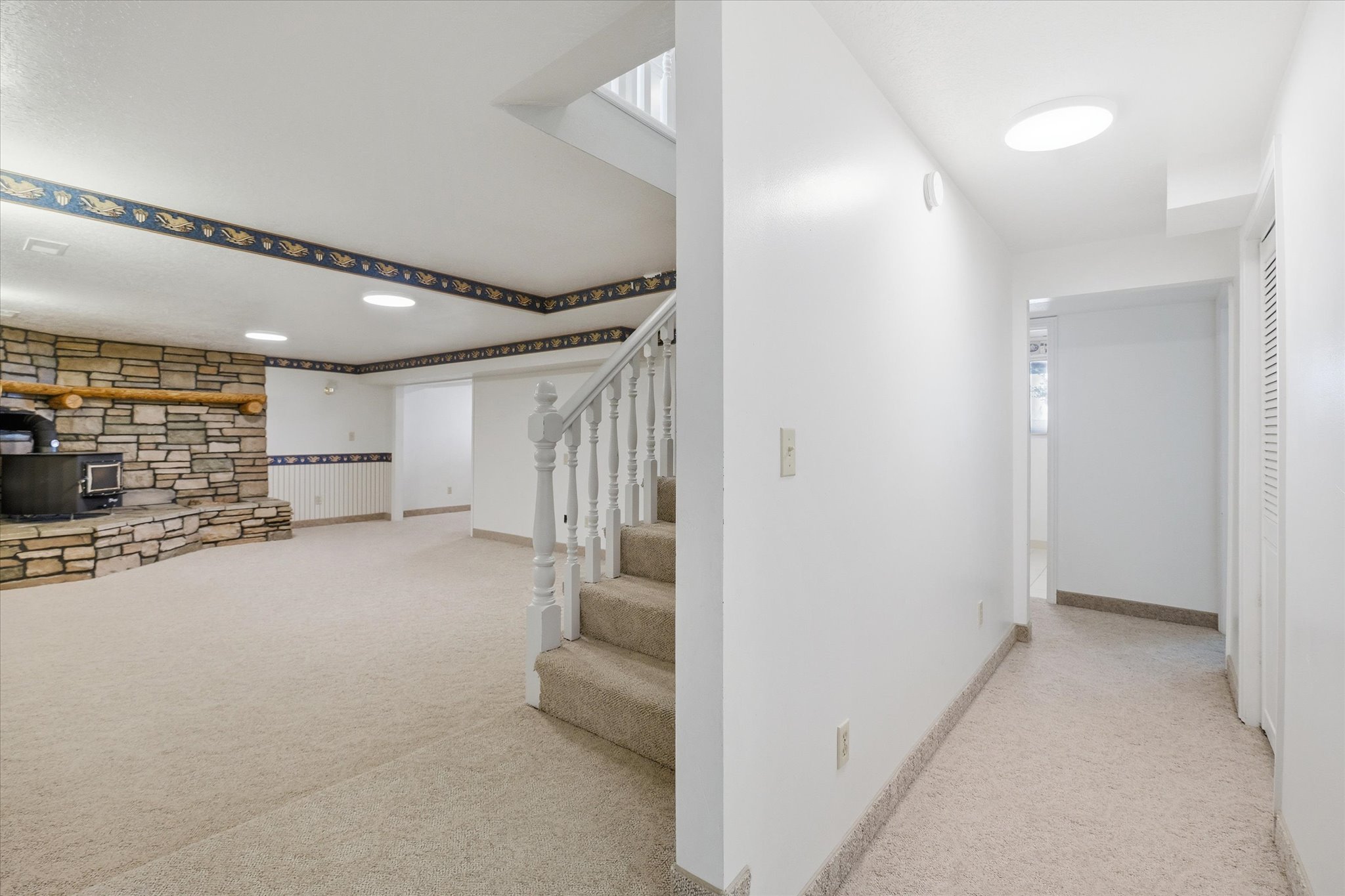 Spacious room featuring a stone fireplace with a log mantel, a wood-burning stove, and neutral-toned carpeting