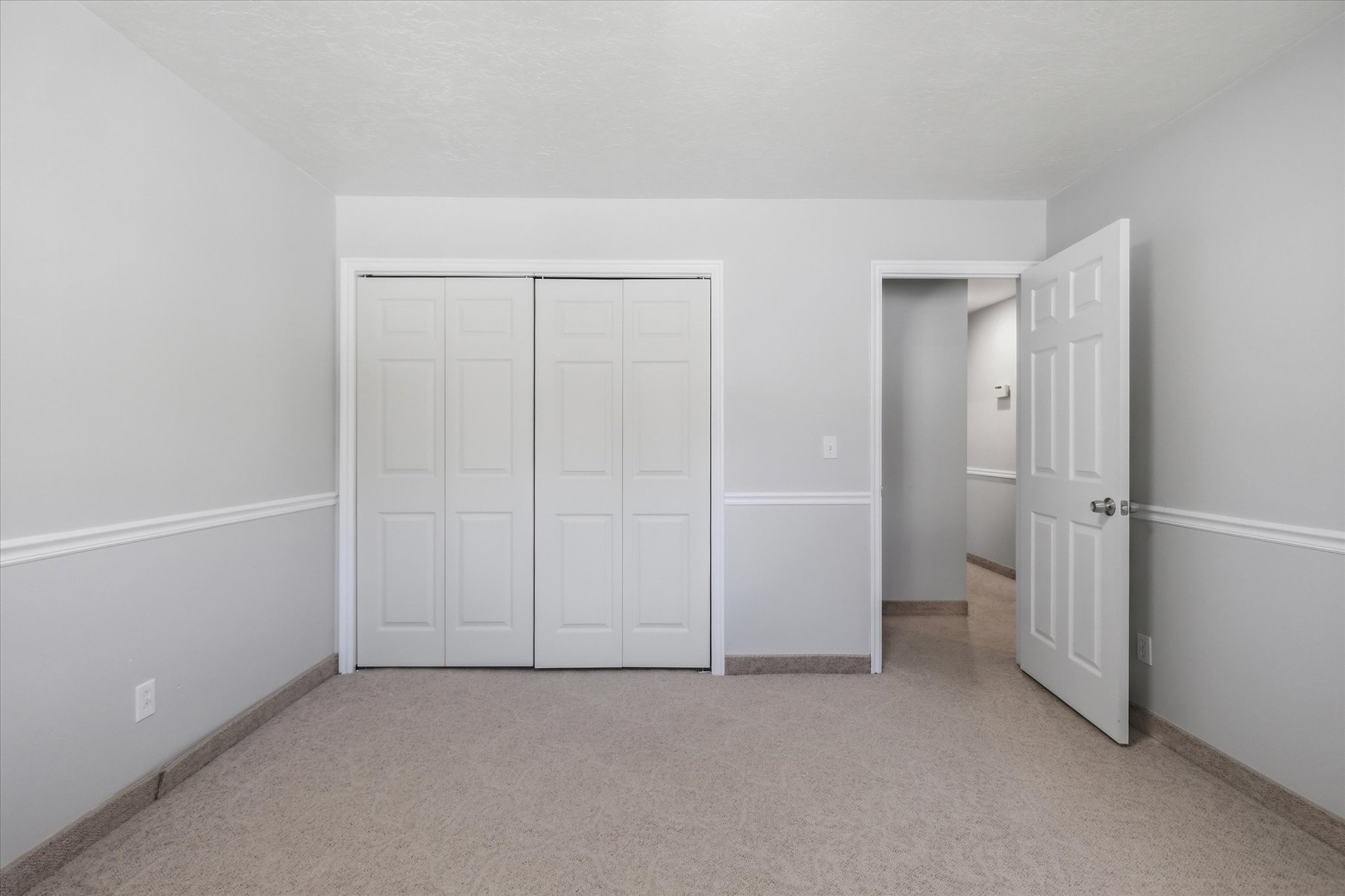 Neutral-toned room featuring a textured carpet floor, chair rail molding, and a closet with bifold doors