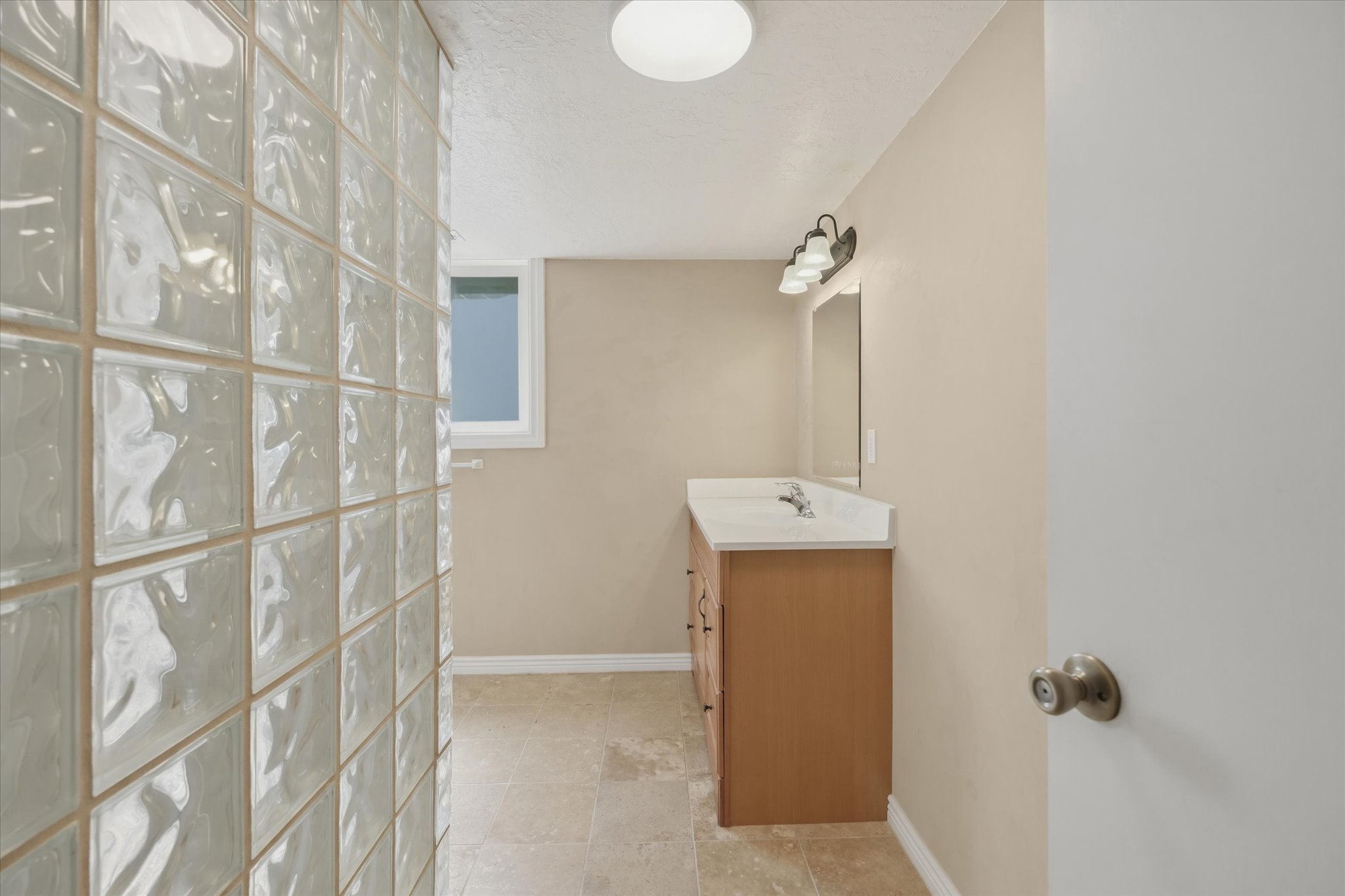 Bathroom featuring a glass block wall, a wood-finish vanity with sink, an integrated countertop, and a wall-mounted light fixture above a mirror