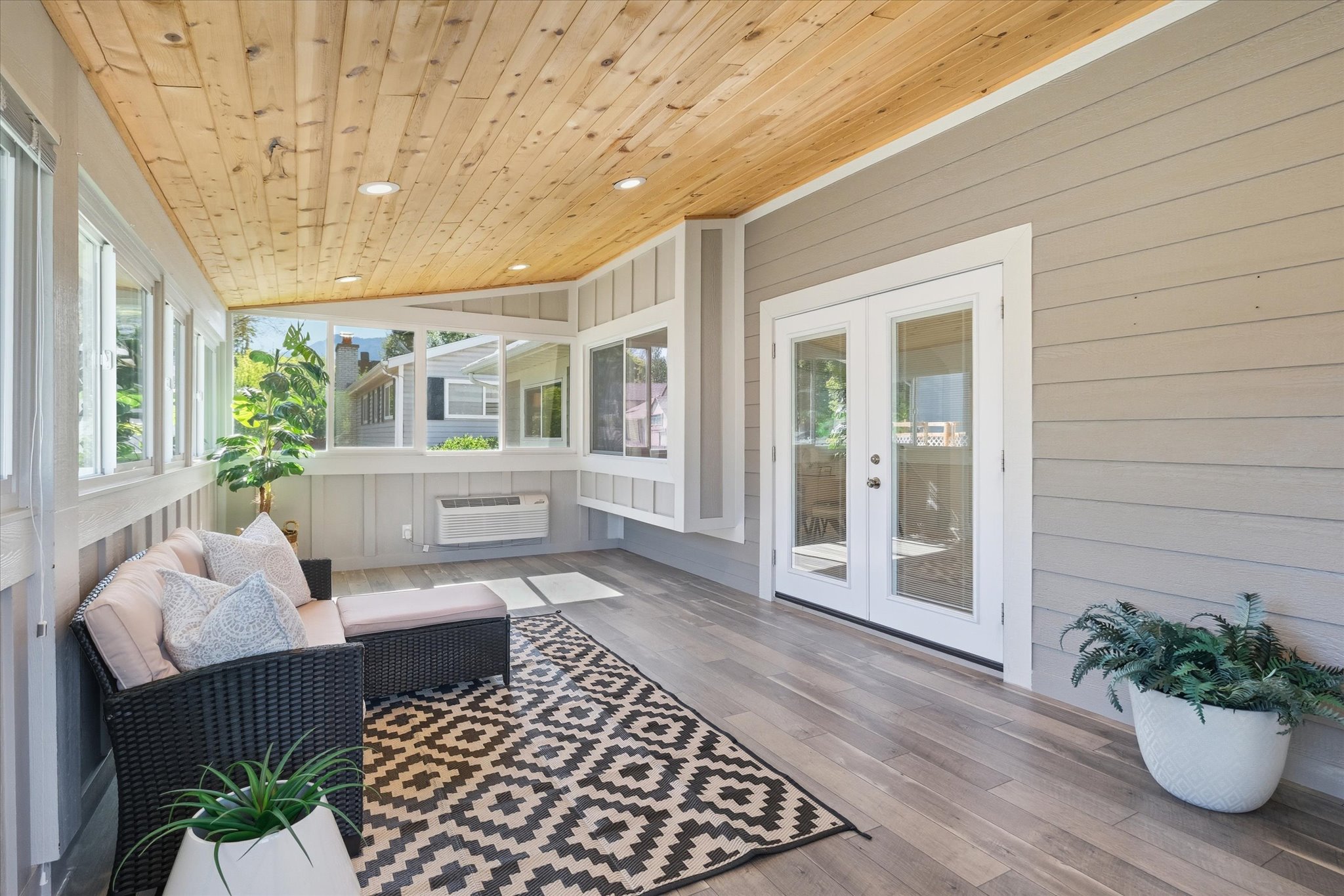 Enclosed sunroom patio featuring a wood-finish plank ceiling with recessed lighting, large windows, and white-framed French doors