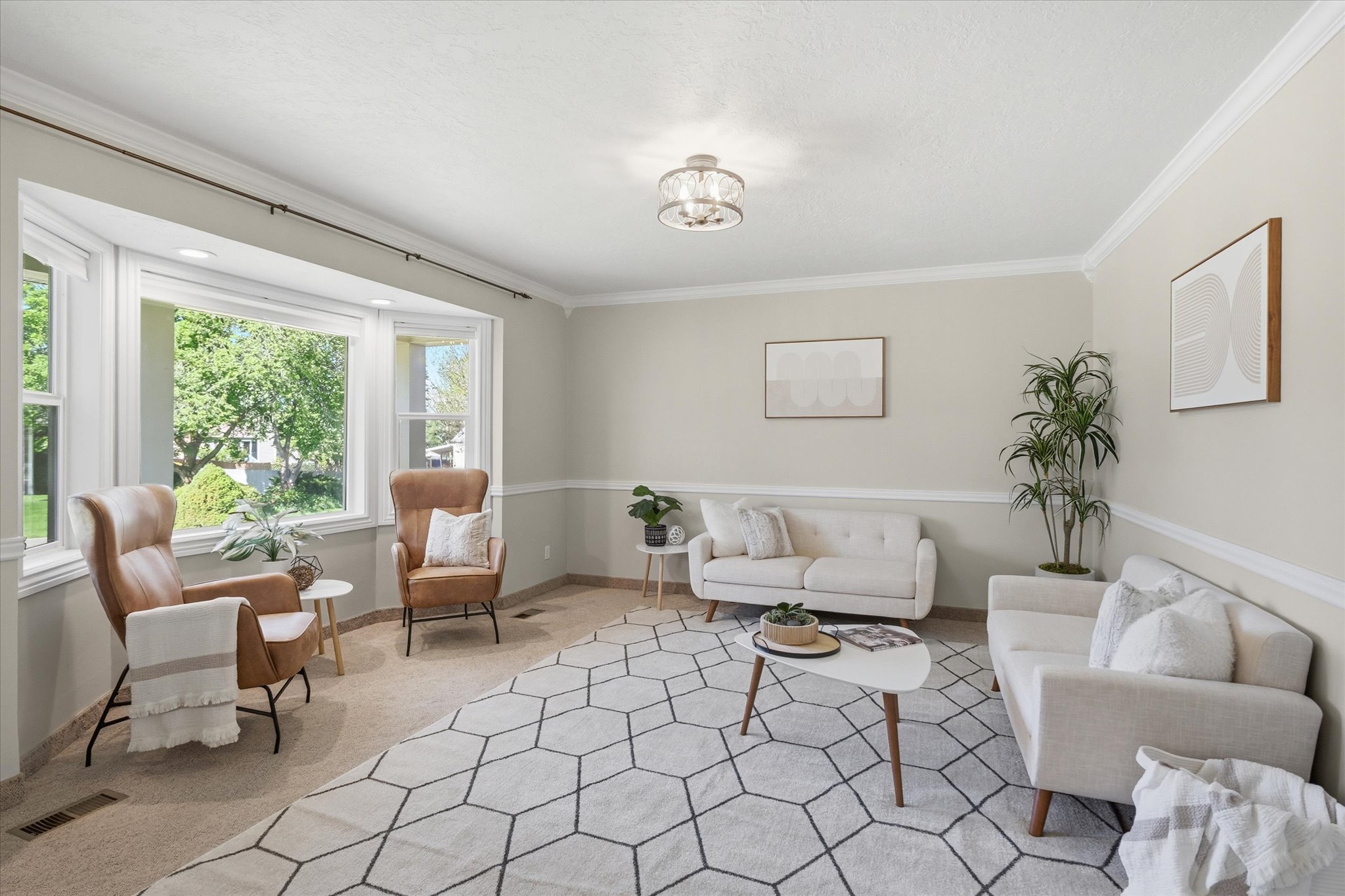 Spacious living area featuring a large bay window, crown molding, chair rail detailing, a contemporary light fixture, and neutral wall tones