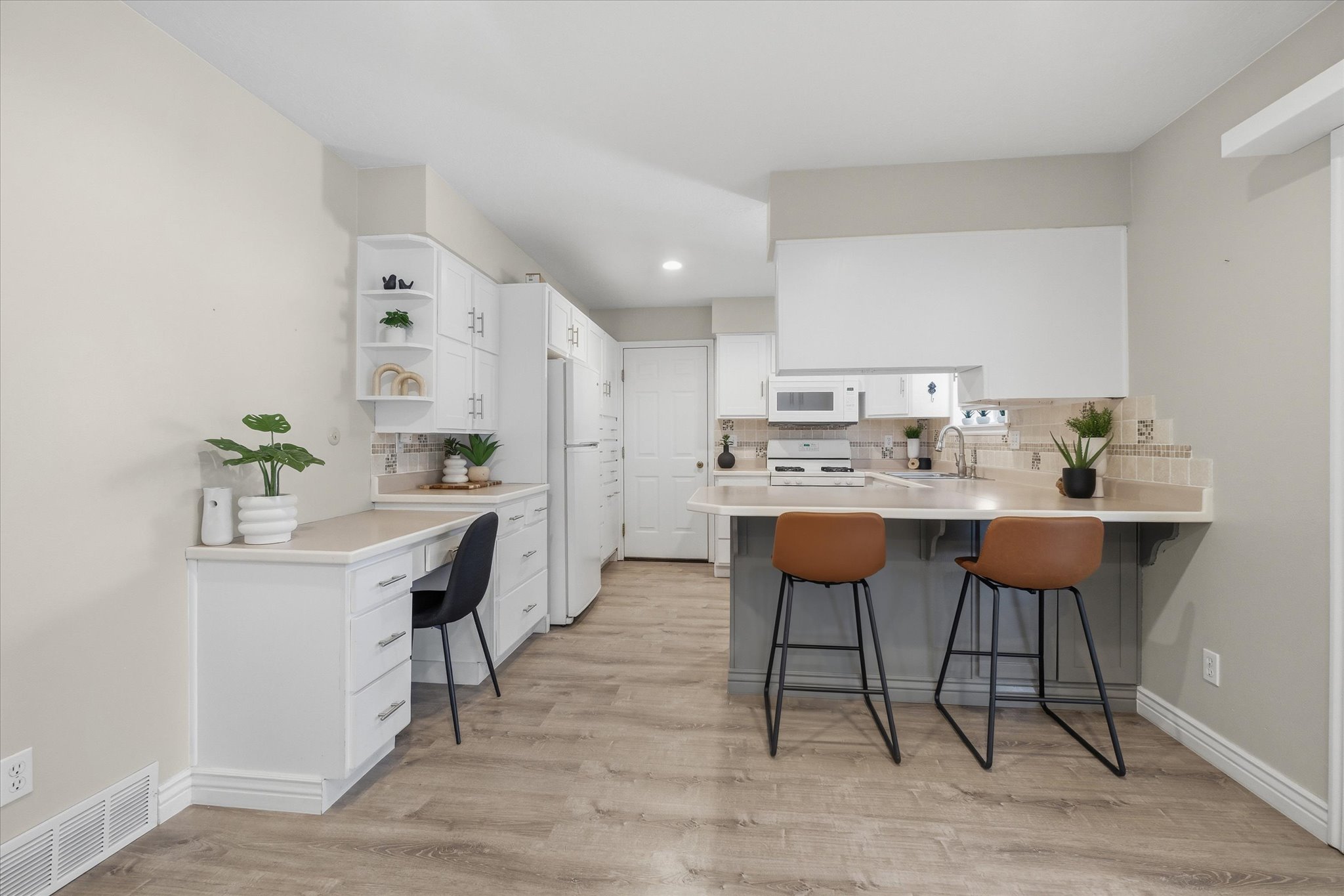 Open-concept kitchen featuring flooring, white cabinetry with silver hardware, a functional built-in desk, and a breakfast bar with an integrated sink