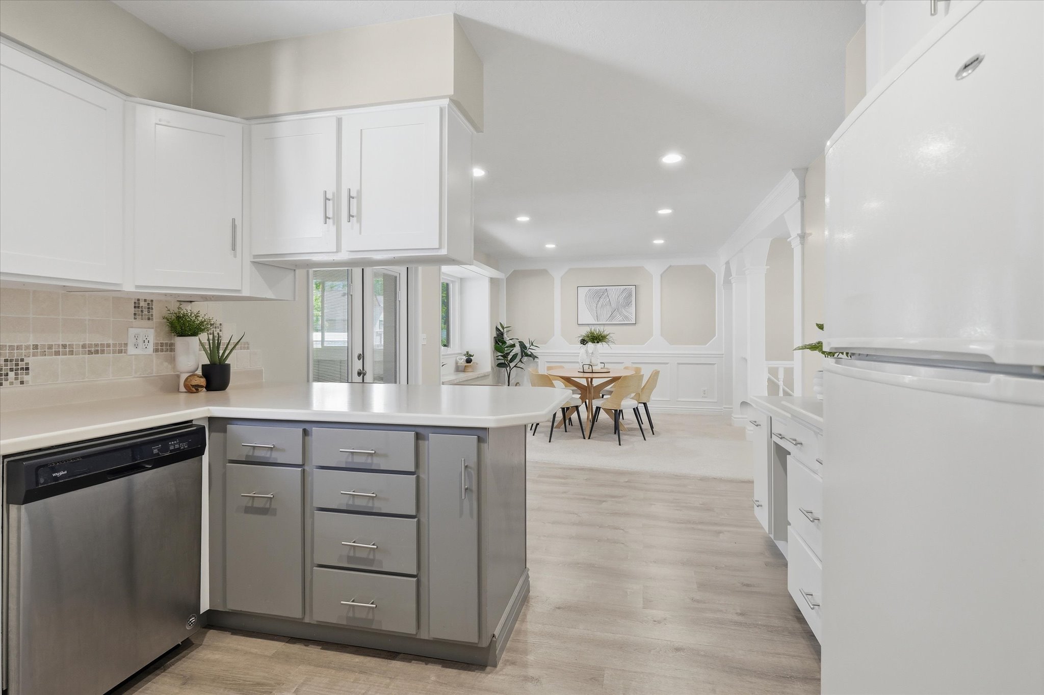 Kitchen featuring white upper cabinetry, gray lower cabinetry, light-toned countertops, and dishwasher