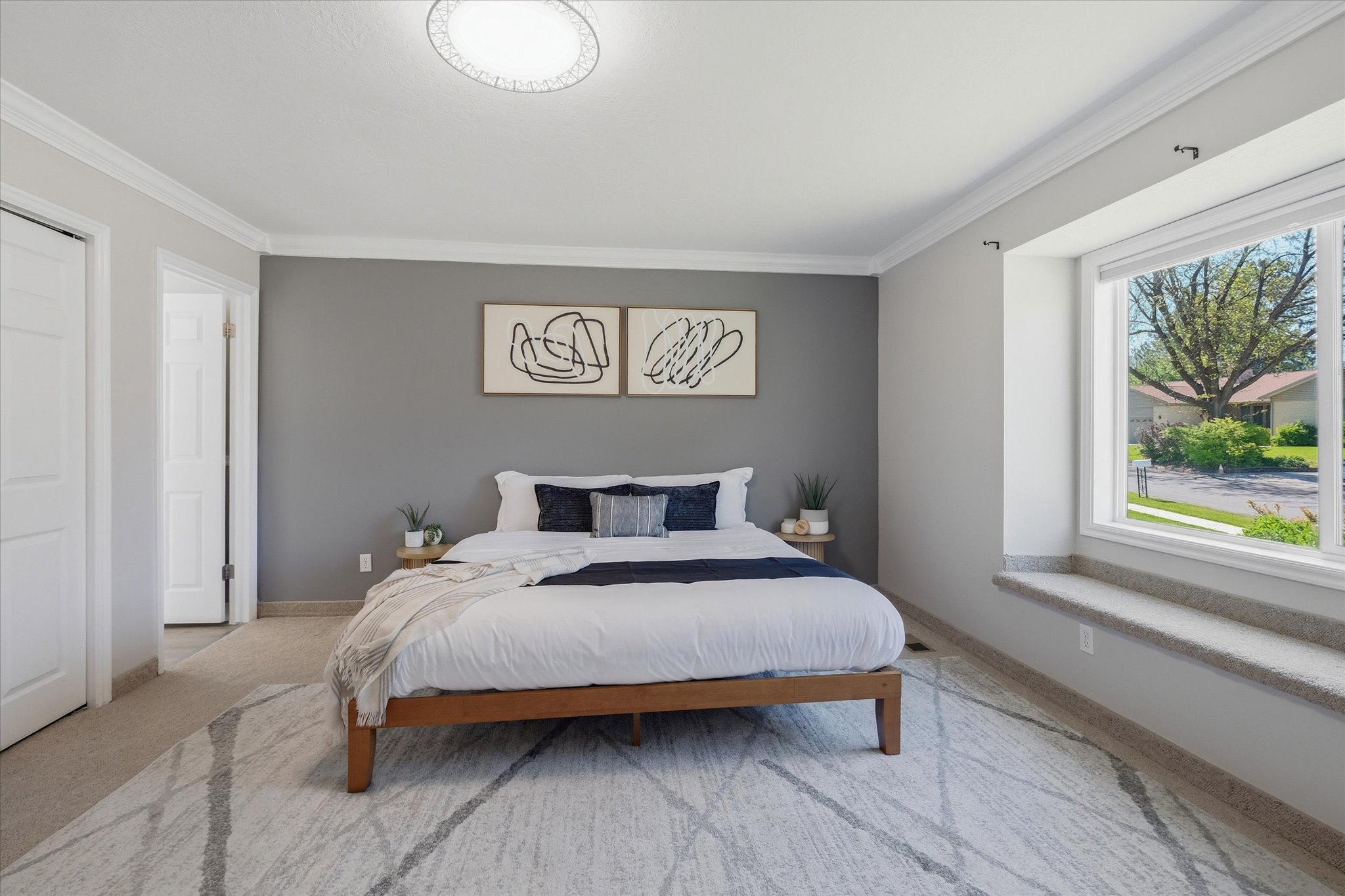 Primary Suite Bedroom carpeted featuring a large picture window with a built-in window seat, crown molding, and a contemporary flush-mount ceiling light fixture