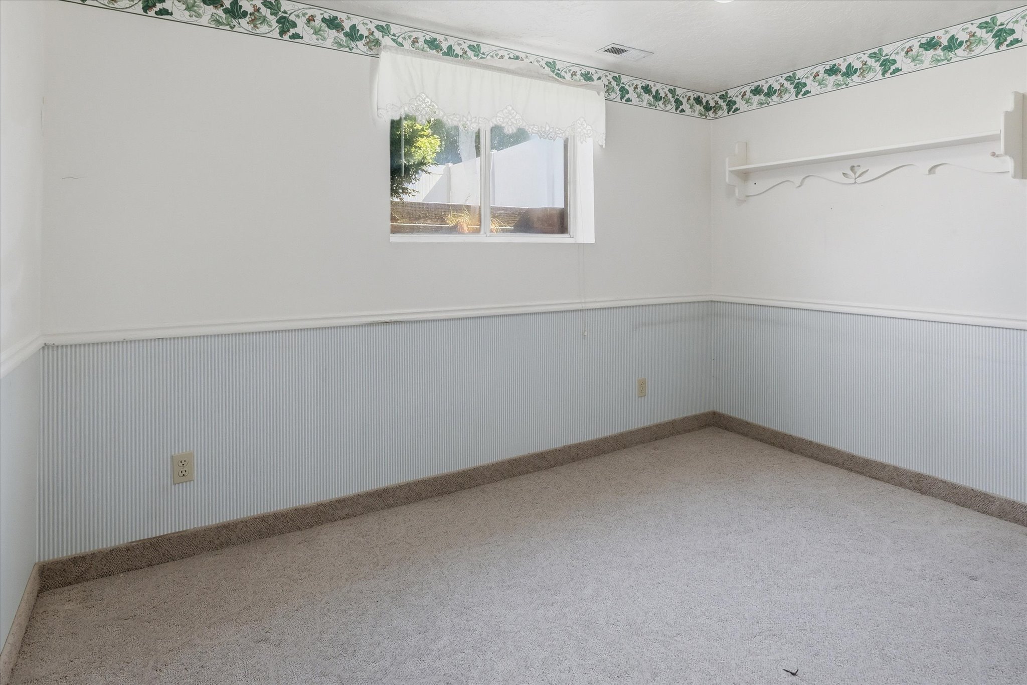 Room featuring a window, light-colored carpeting, white walls, light blue striped wainscoting, and a decorative wall border