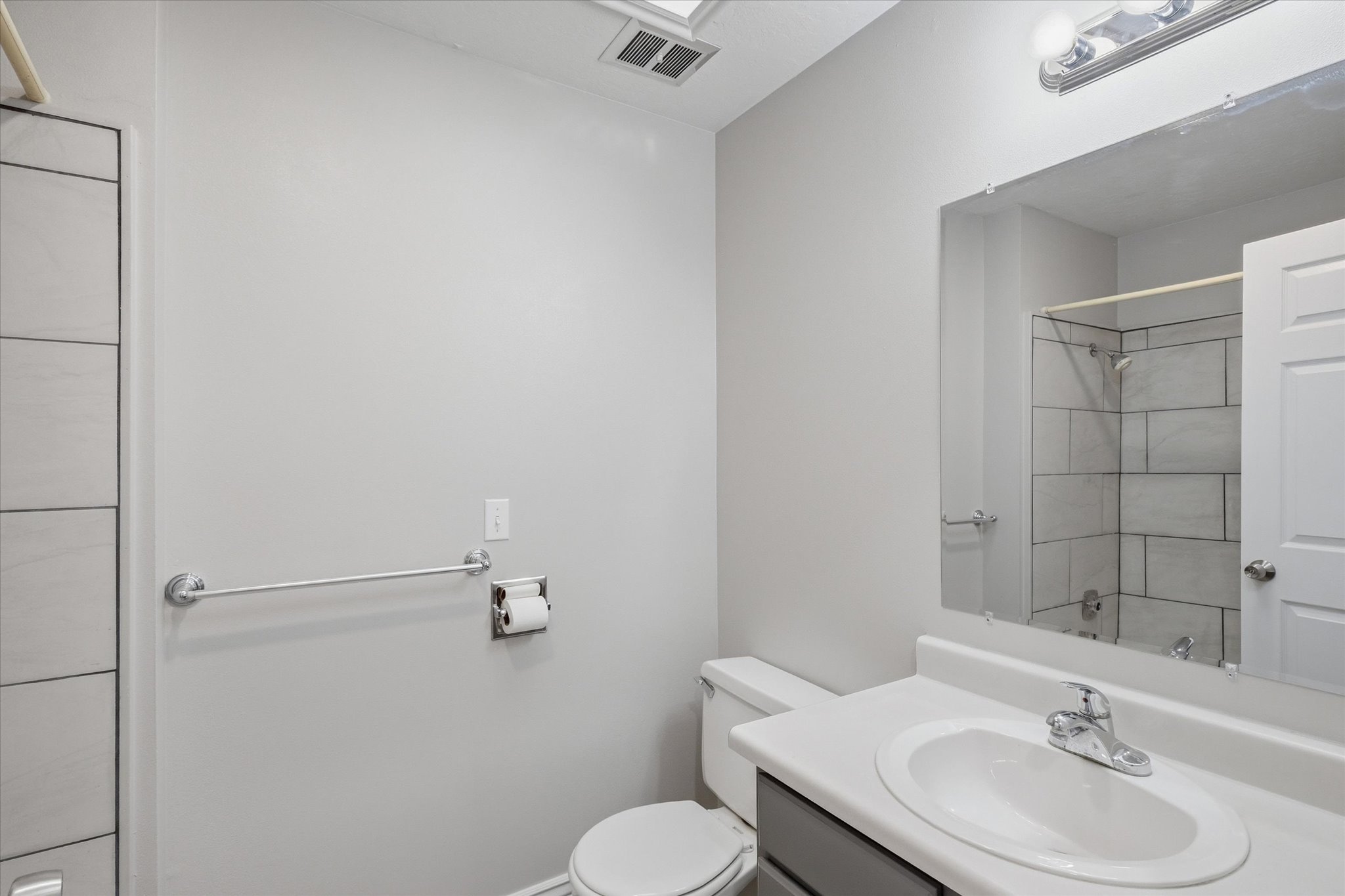 Bathroom featuring a vanity with an integrated sink, a rectangular mirror, a shower with tiled walls, and a recessed ceiling light