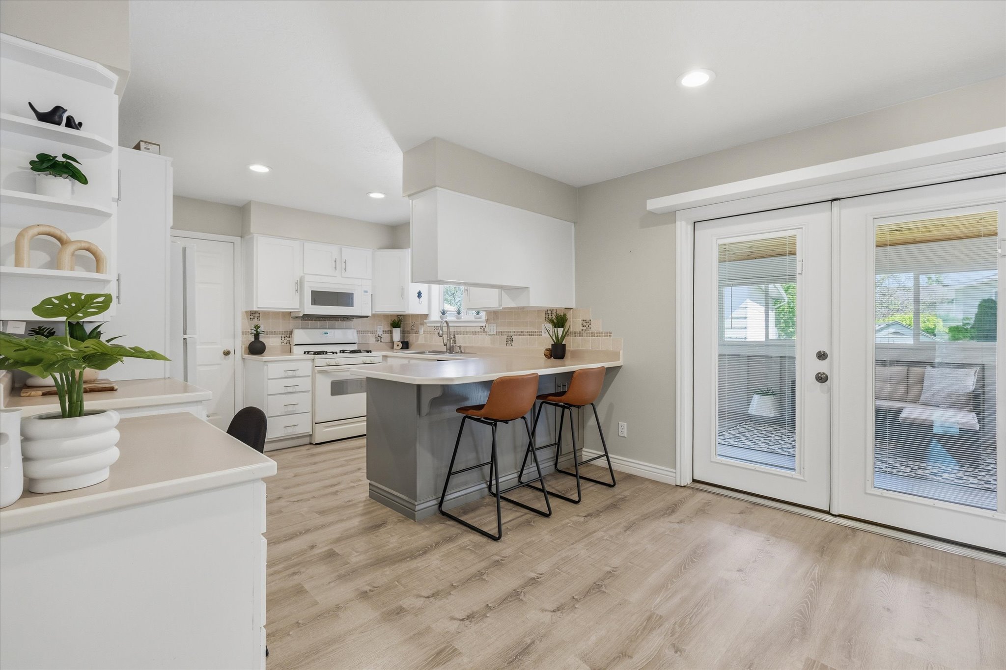 Bright kitchen featuring light flooring, white cabinetry, recessed lighting, a breakfast bar, and double glass-paneled doors leading to an outdoor space