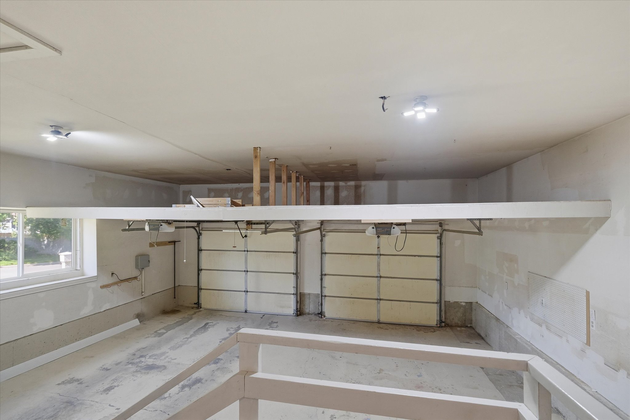 Two overhead garage doors with automatic openers, concrete flooring, and an elevated storage platform