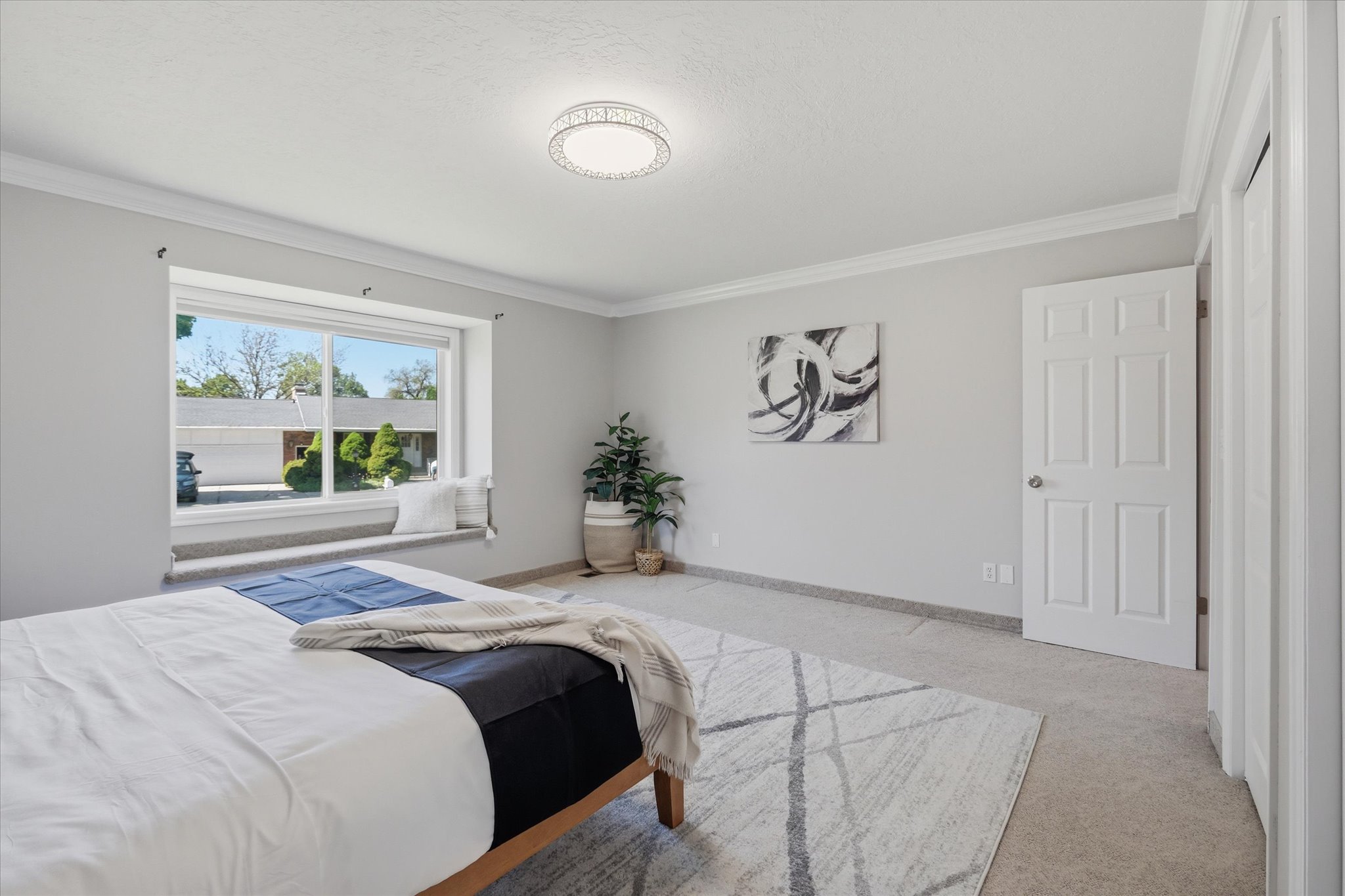 Spacious Primary Suite Room featuring a large window with a built-in window seat, crown molding, a decorative ceiling light fixture, and carpet flooring