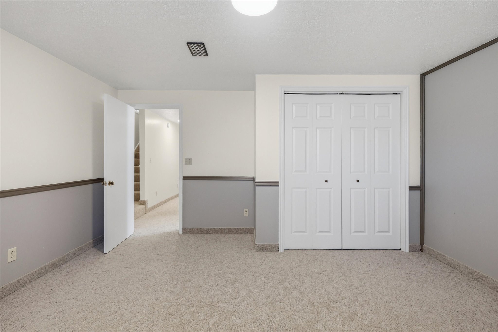 Carpeted room featuring a neutral color palette, bi-fold closet doors, white trim, and a partial view of a staircase