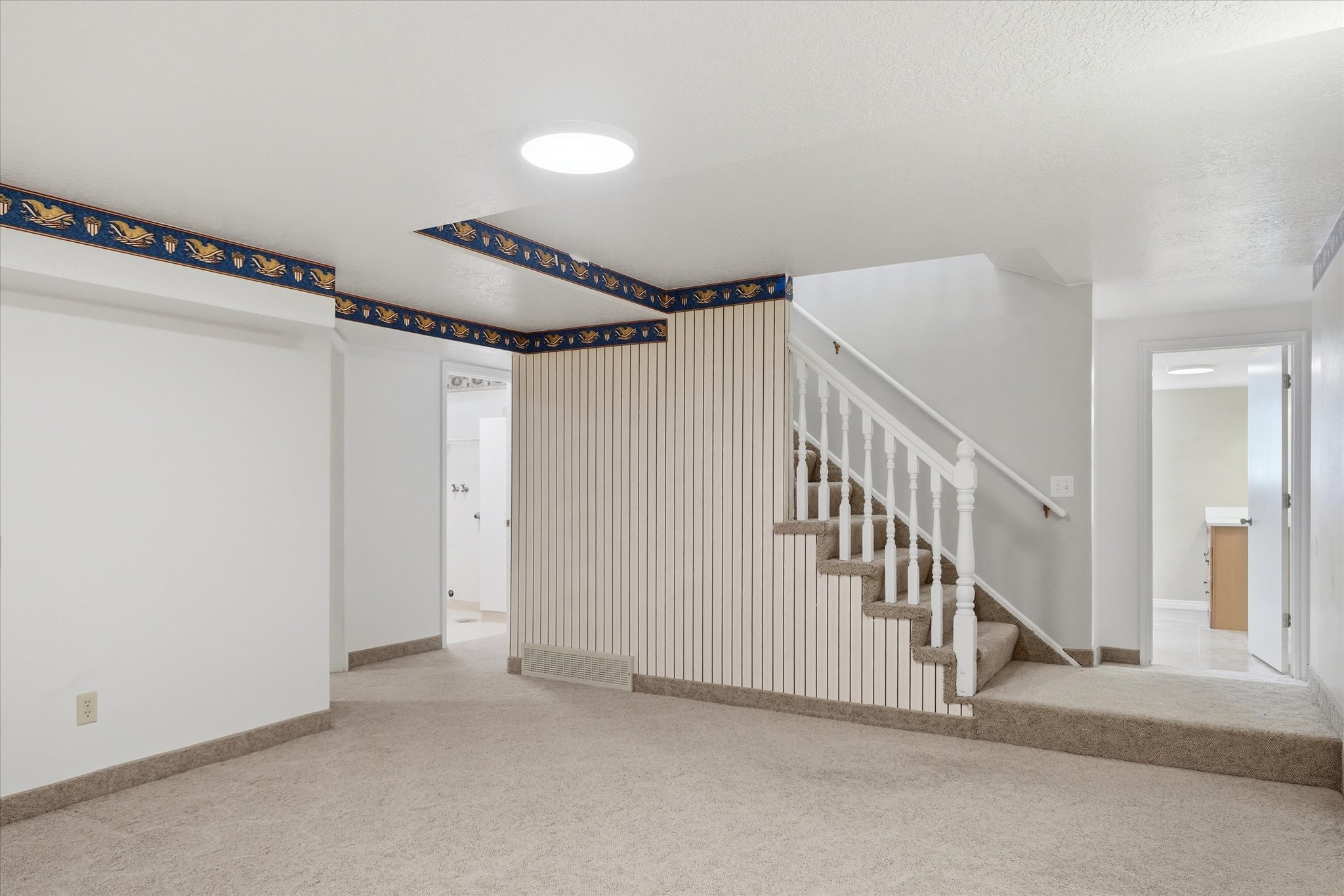 Carpeted interior space featuring a staircase with white railings, a light fixture, and white walls