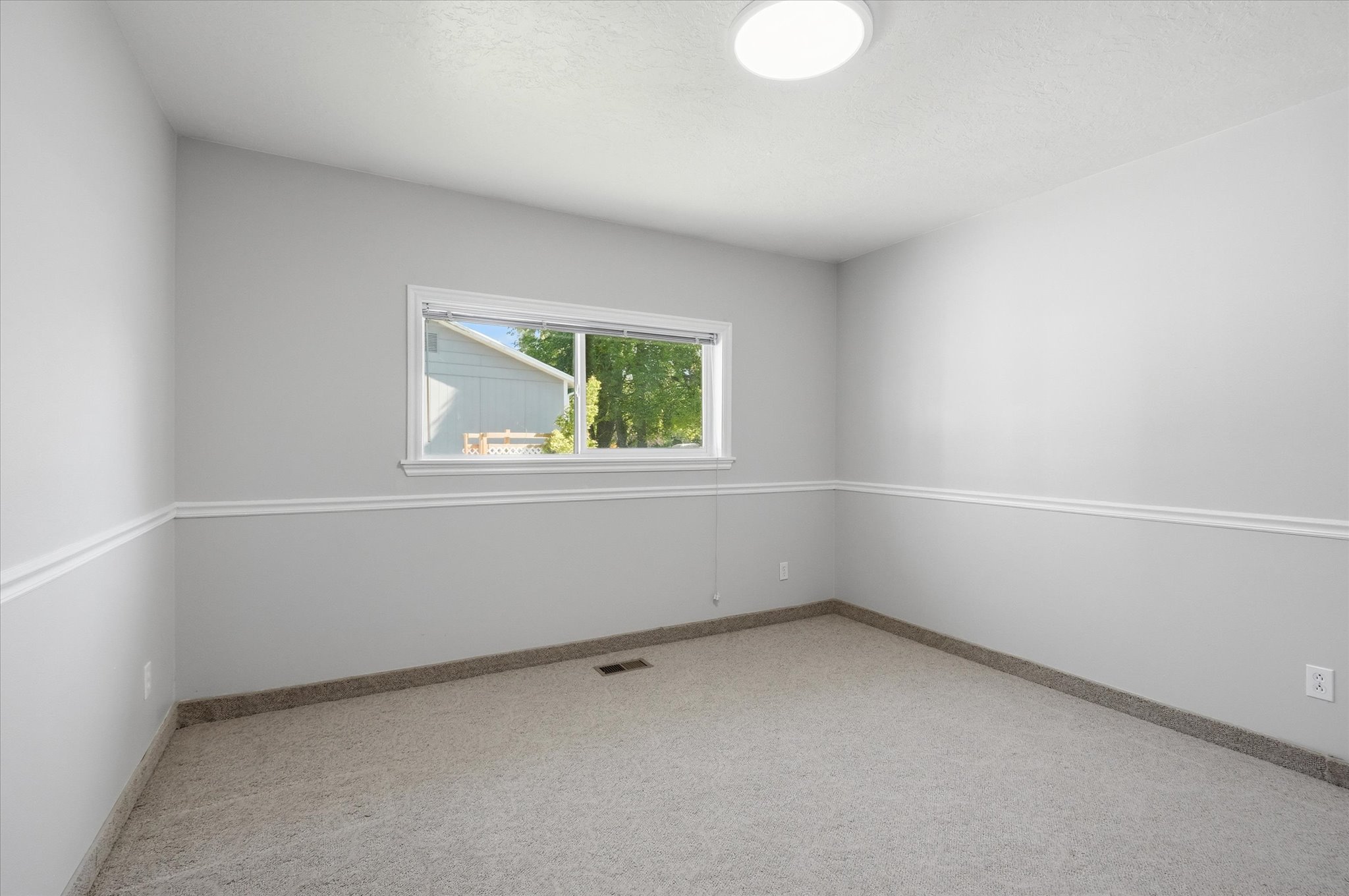 Neutral-toned room featuring a single window, light gray walls with chair rail molding, a white ceiling, and light-colored carpet flooring