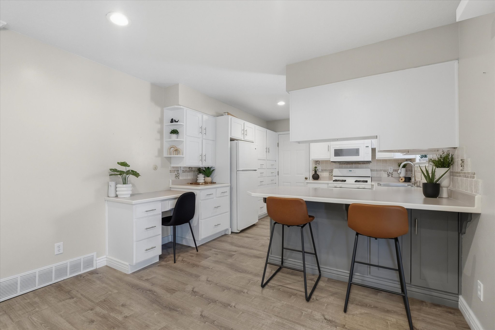 Kitchen featuring flooring, white cabinetry, a built-in desk area, a breakfast bar with contrasting base cabinetry, and a tile backsplash