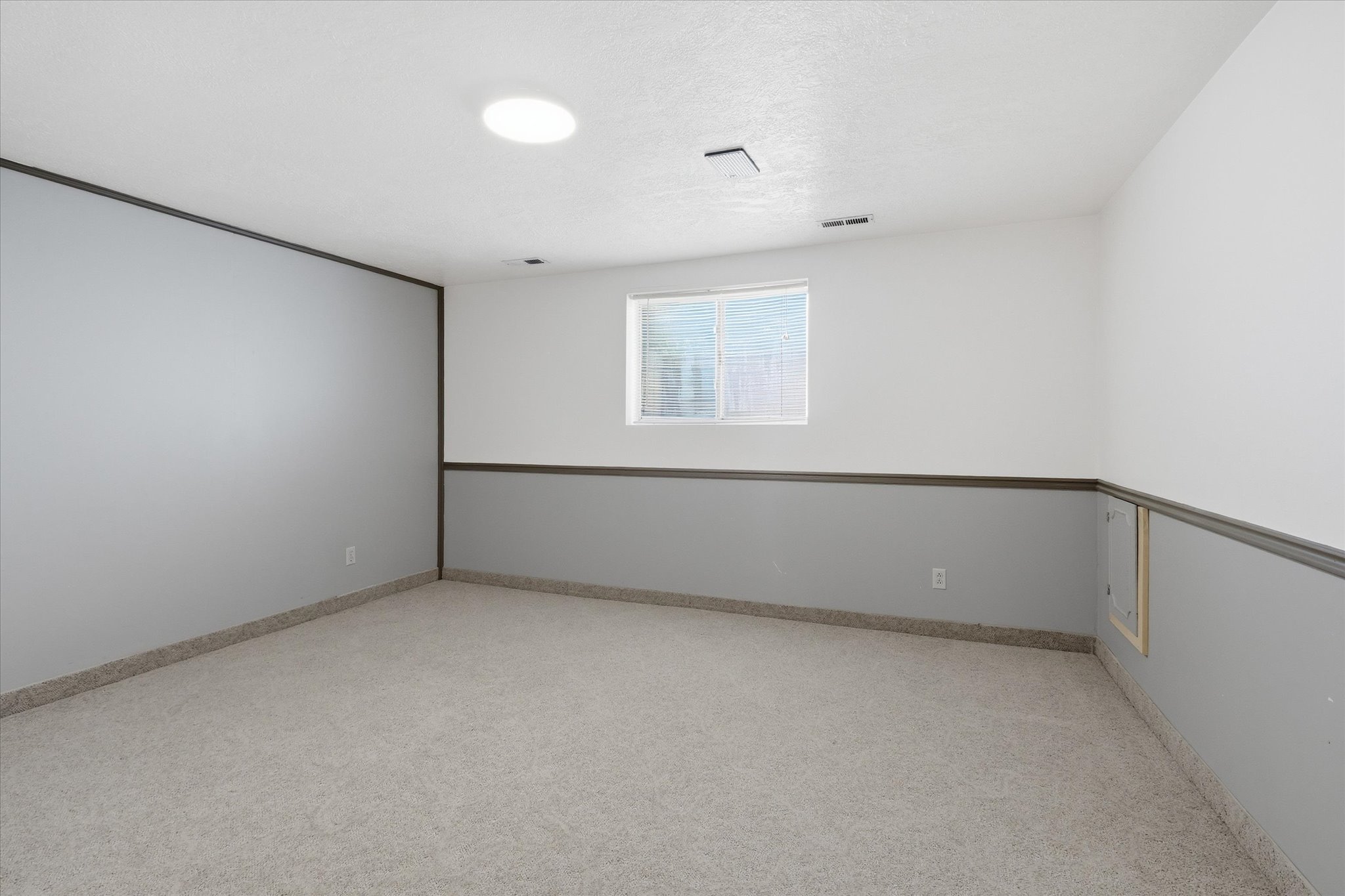 Spacious room featuring a neutral color palette and a two-tone wall treatment with a gray wainscoting