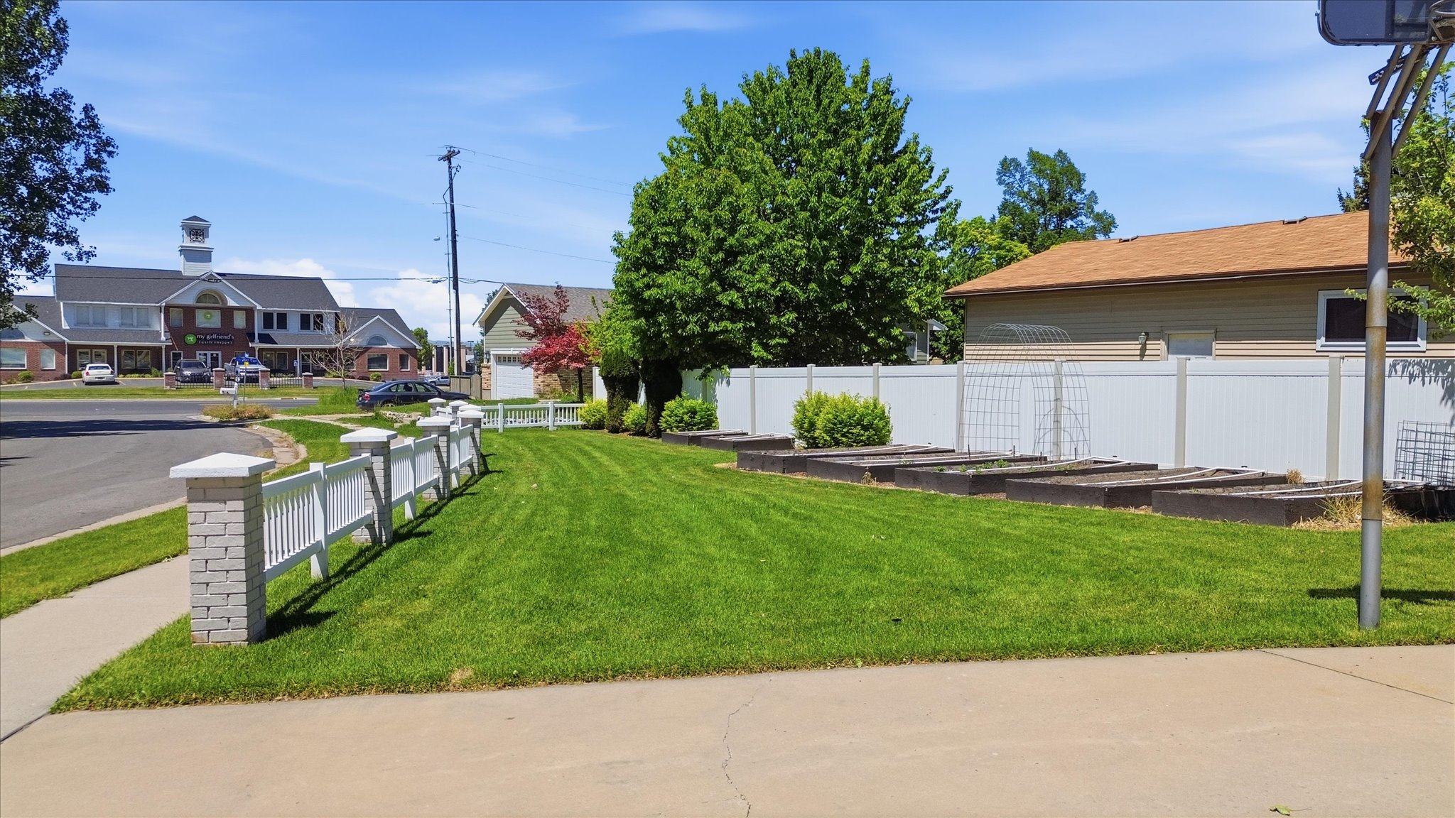 Front yard featuring a white picket fence with stone pillars, a lush green lawn, and raised garden beds