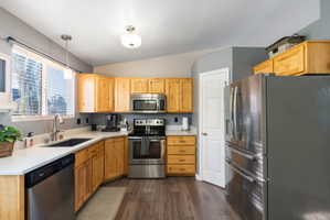 Kitchen featuring natural wood cabinetry, stainless steel appliances, a deep basin sink, and wood-finish flooring