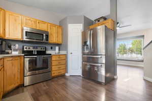 Kitchen featuring wood cabinetry, stainless steel appliances including a refrigerator, range, and microwave, and wood-finish flooring