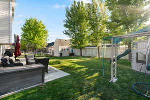 Spacious backyard featuring a concrete patio, expansive lawn, mature trees, and a white privacy fence