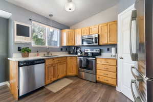 Kitchen featuring wood cabinetry, stainless steel appliances, light-toned countertops, a window with blinds, and wood-finish flooring