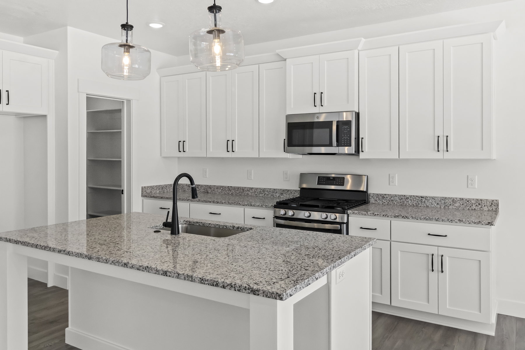 Kitchen featuring an oversized island with an undermount sink and matte black faucet, white shaker cabinetry, stainless steel appliances
