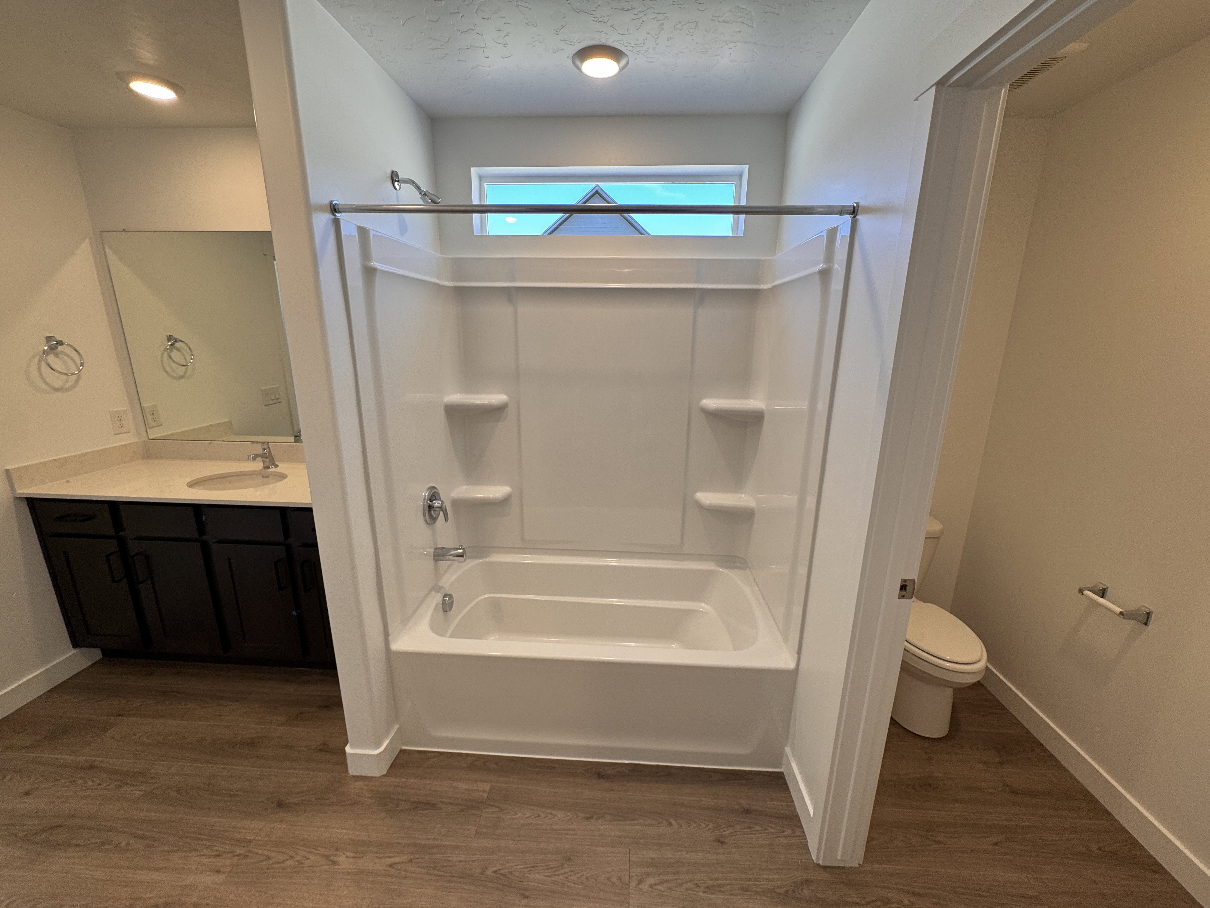 Bathroom featuring a white tub/shower combination with integrated shelving, chrome fixtures, and a transom window
